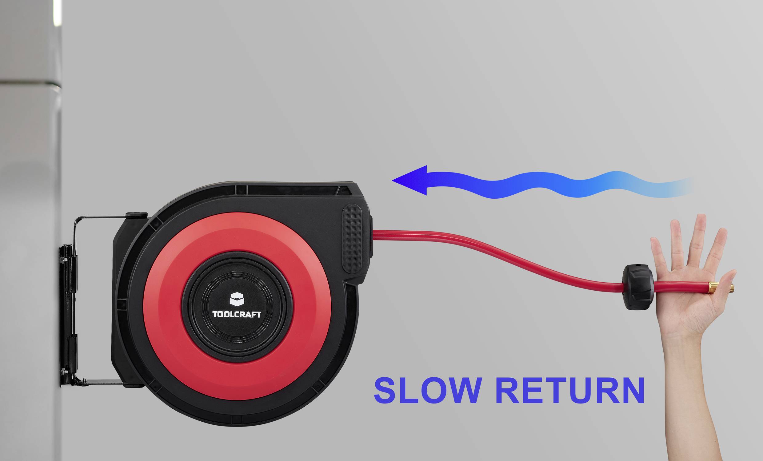 Eine Hand zieht einen roten Schlauch von einer wandmontierten Rolle mit der Bezeichnung „LANGSAME RÜCKFÜHRUNG