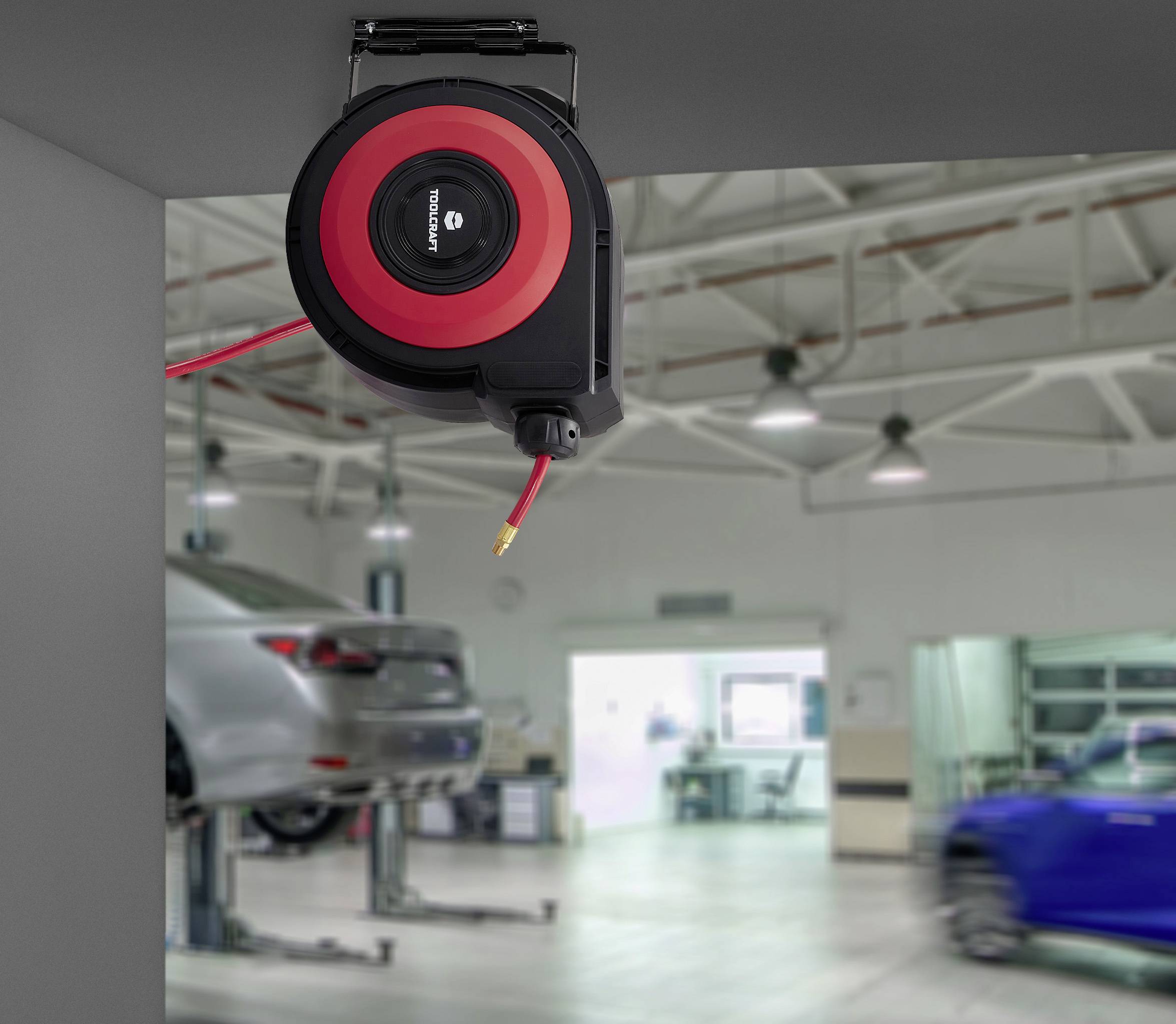 Eine einziehbare Schlauchrolle mit rotem und schwarzem Gehäuse ist an der Decke einer Garage montiert. Im Hintergrund sind Autos in einer geräumigen Werkstatt angehoben.