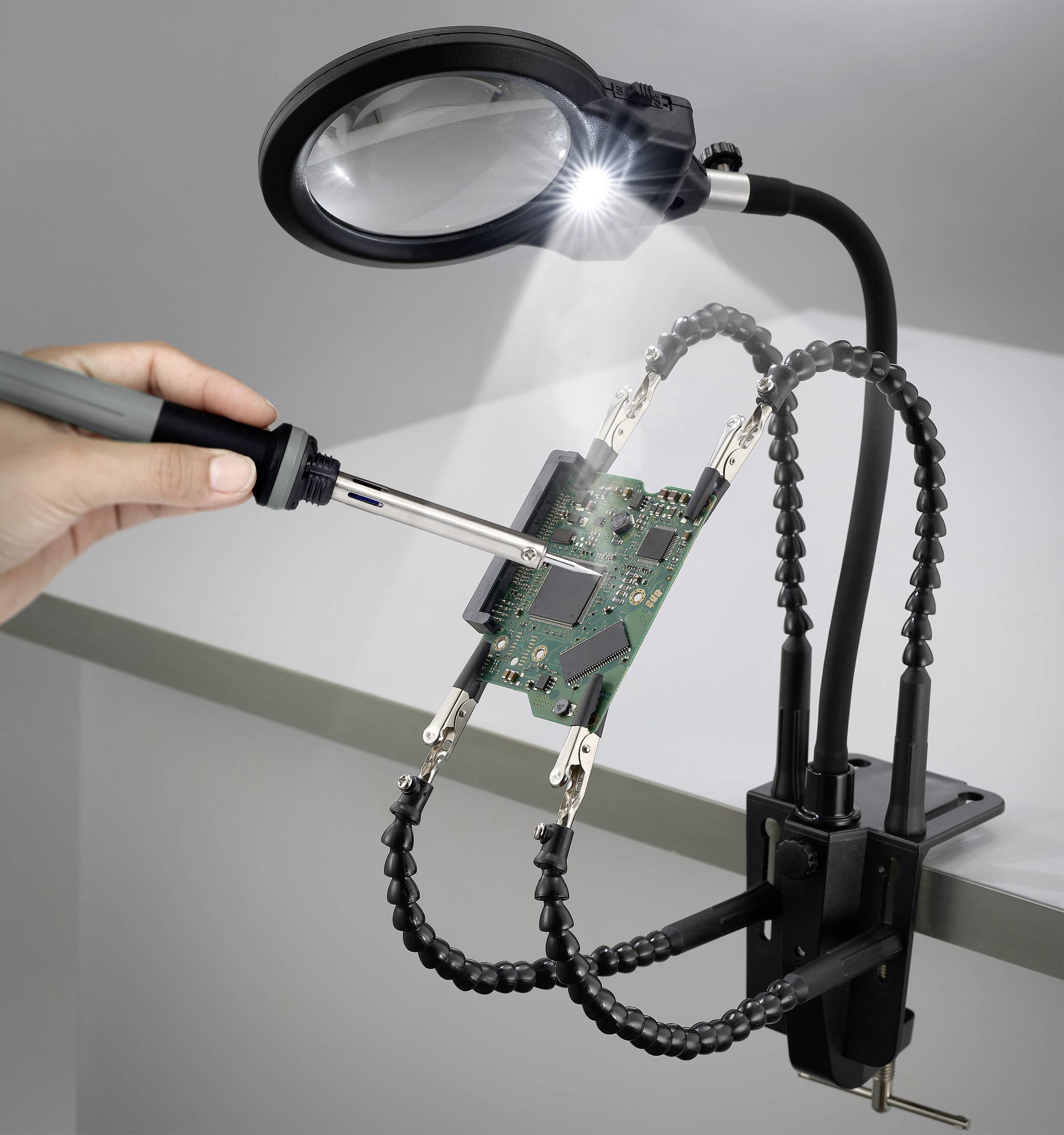 Eine Person lötet eine Leiterplatte, die von einem flexiblen Klemmständer mit angebrachter Lupe und Beleuchtung gehalten wird, und demonstriert dabei elektronische Arbeiten.
