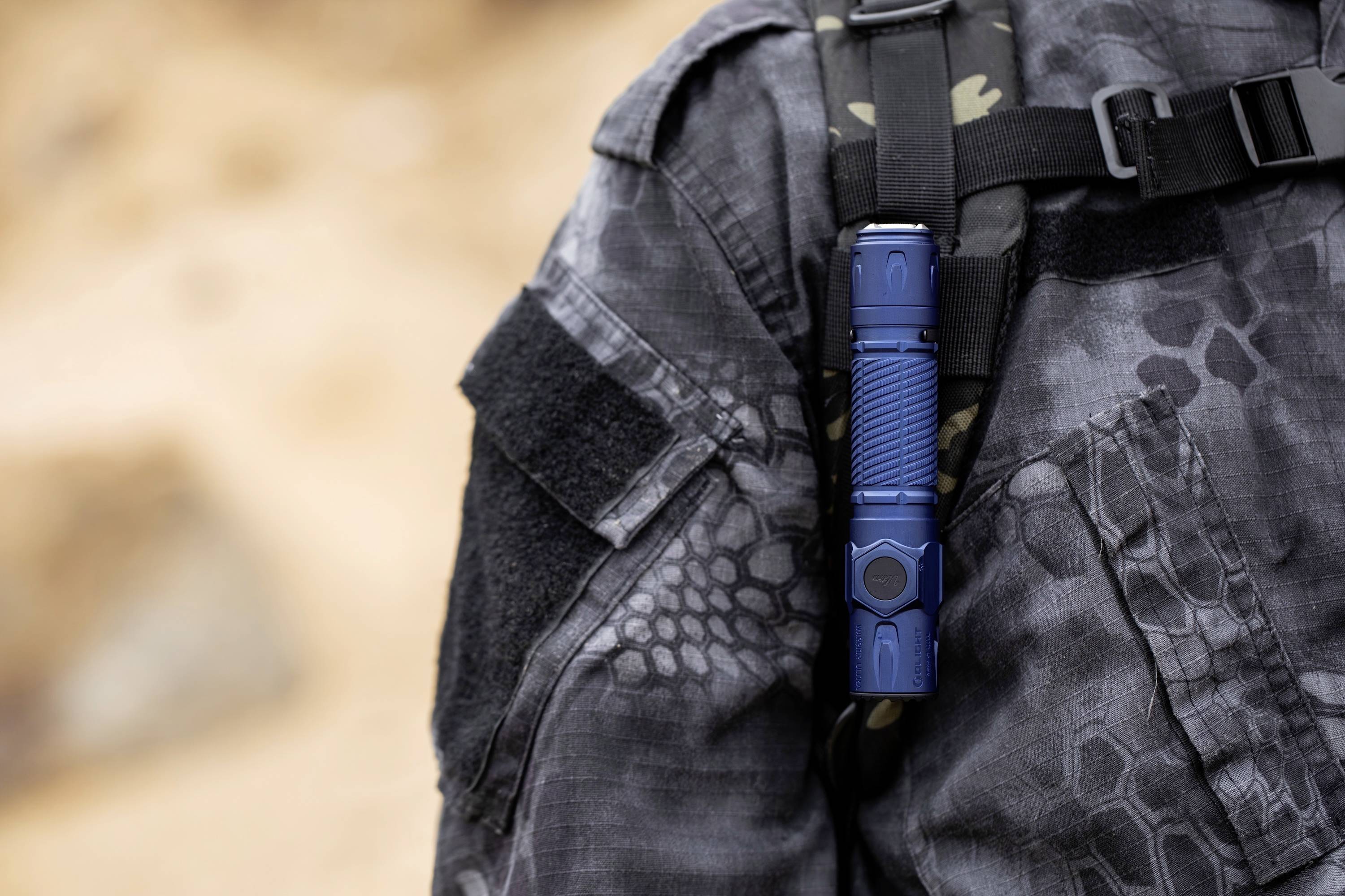 Eine Taschenlampe ist am Brustgurt einer Person mit einer taktischen Jacke in Grau-Camouflage befestigt, was die Bereitschaft für Aktivitäten im Freien signalisiert.