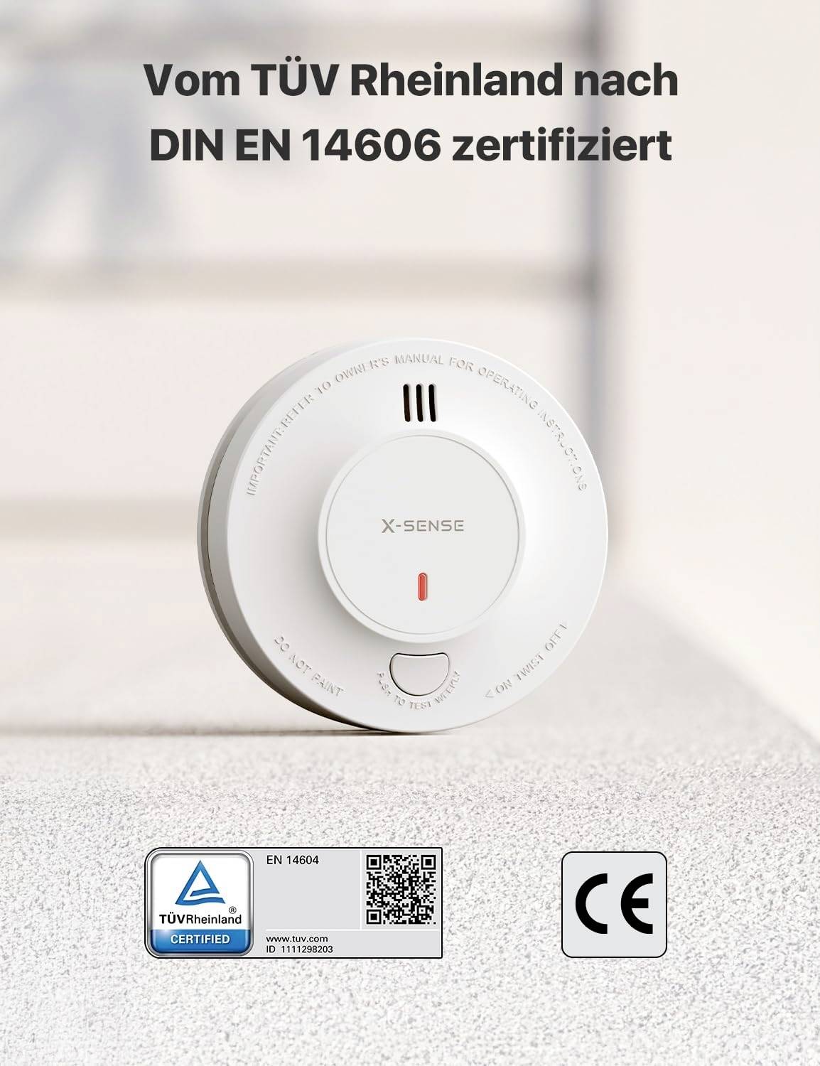 Rauchmelder auf einem Tisch. Text oben: 'Vom TÜV Rheinland nach DIN EN 14606 zertifiziert'. Unten: TÜV, QR-Code, CE-Symbol.