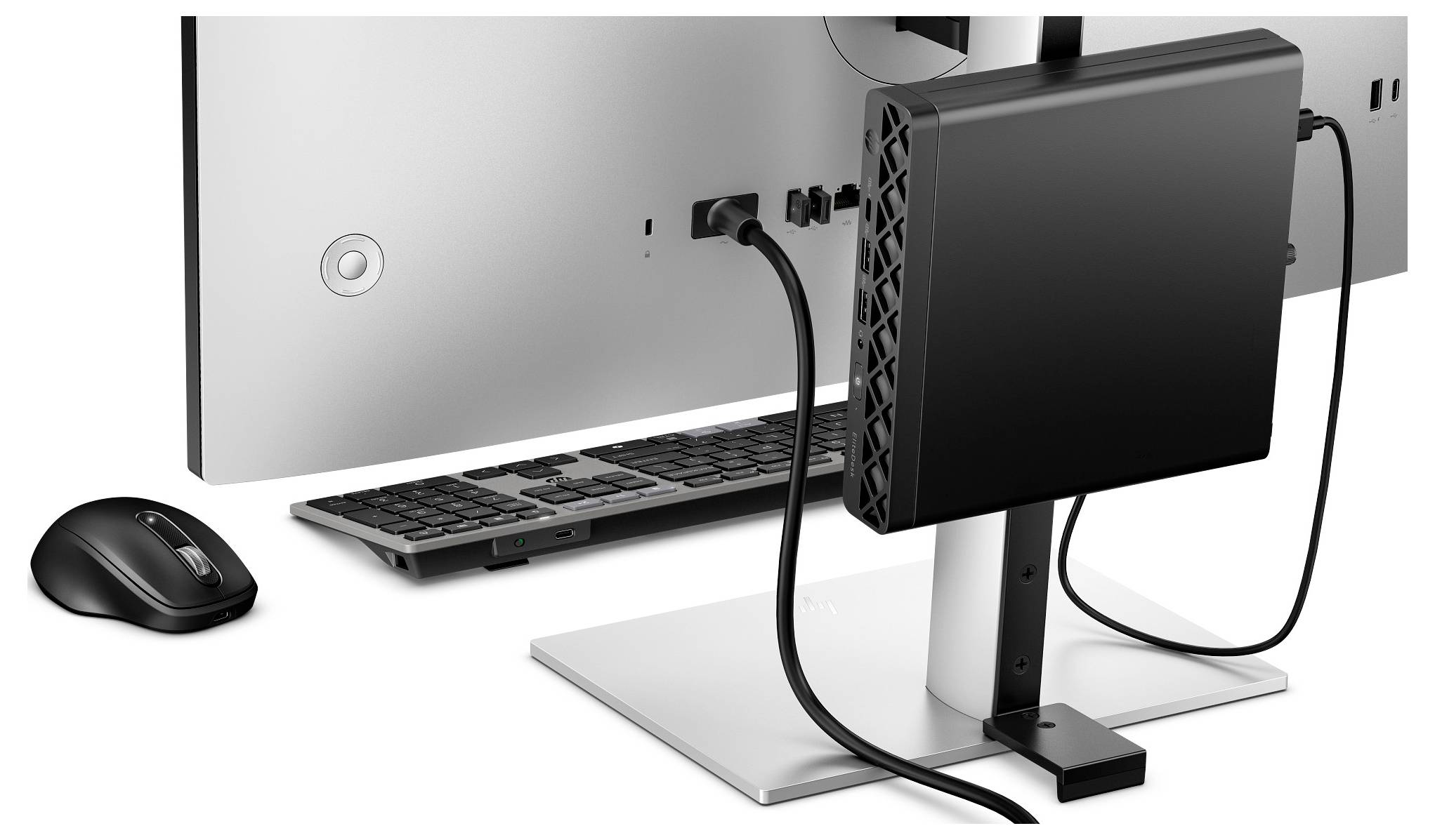 Ein Computermonitor mit einem Thin Client und verschiedenen Kabeln, die an der Rückseite angeschlossen sind, zusammen mit einer drahtlosen Tastatur und Maus auf einem Schreibtisch.