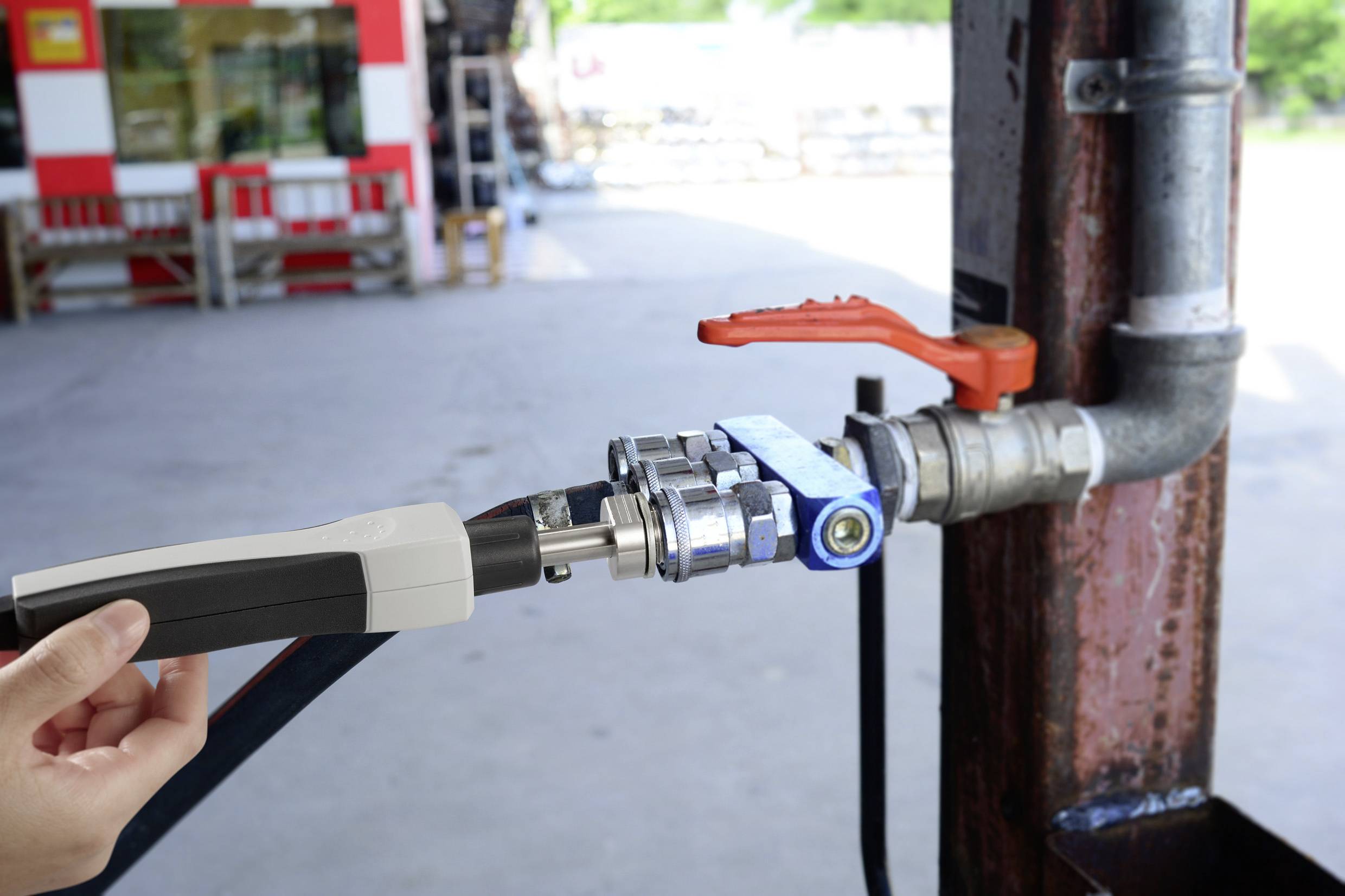 Eine Person hält eine Zapfpistole an einer Tankstelle, was darauf hindeutet, dass sie gerade tankt oder Wartungsarbeiten durchführt.
