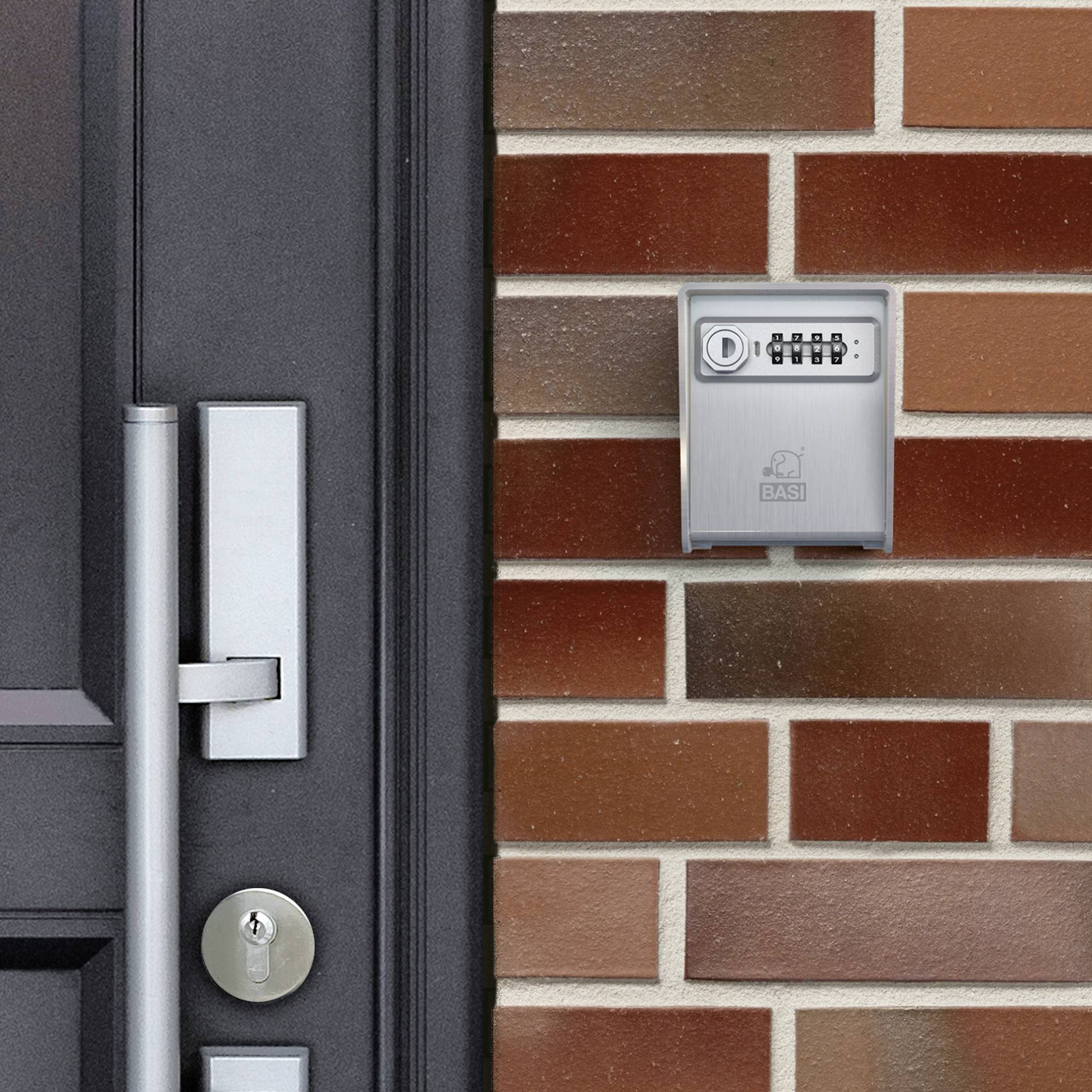 Ein silberner digitaler Zahlenschloss-Tresor ist an einer roten Ziegelwand neben einer schwarzen Tür mit einem modernen Griff montiert.