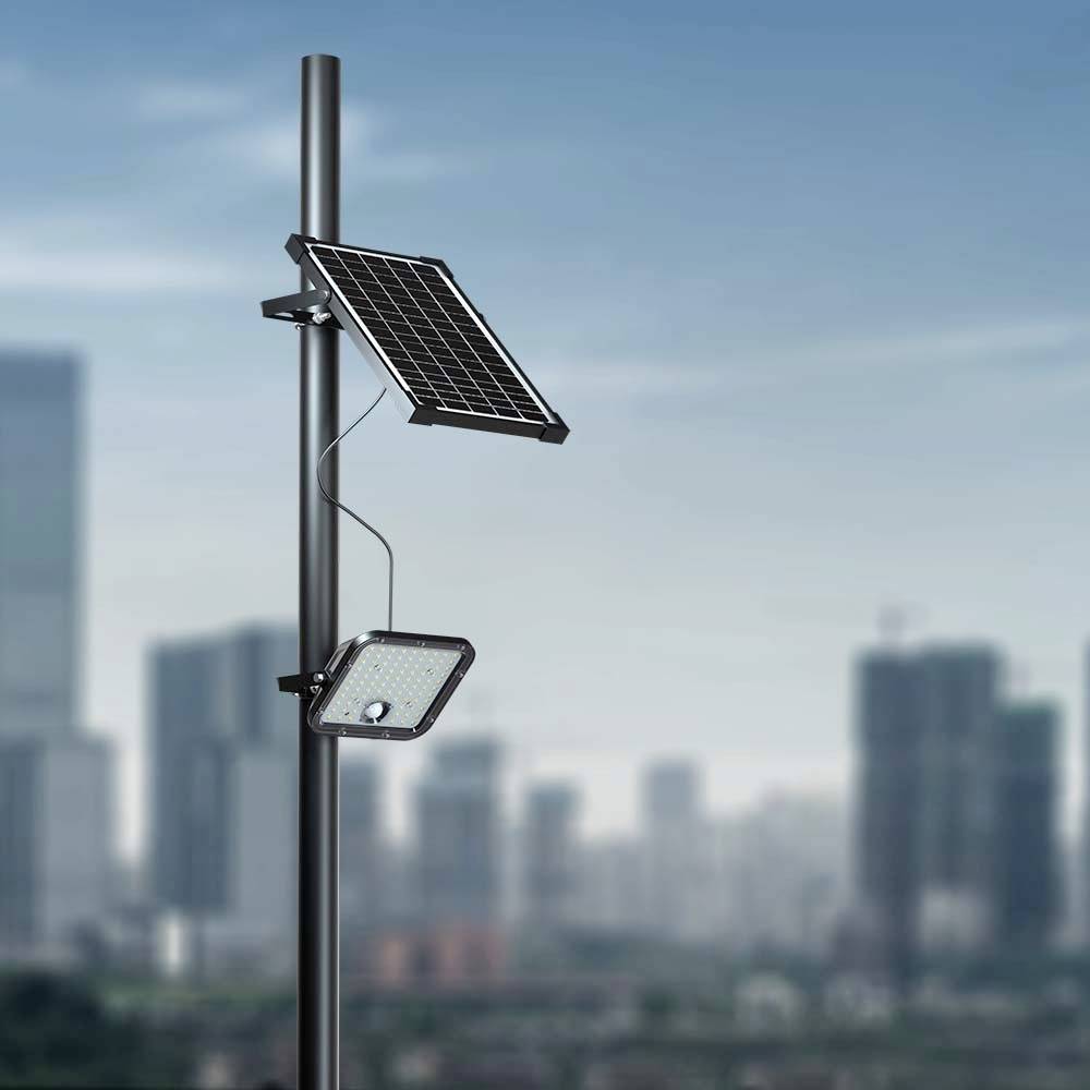 Eine Straßenlaterne mit Solarpanel ragt hoch vor einer Stadtsilhouette von Wolkenkratzern unter einem klaren blauen Himmel.