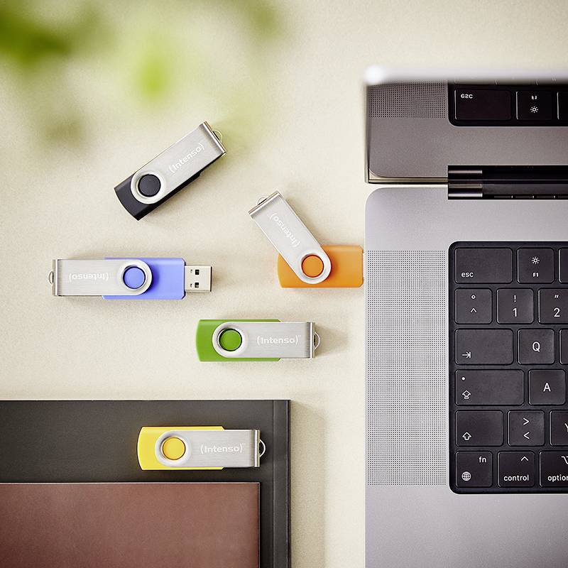 USB-Sticks in verschiedenen Farben sind auf einem Schreibtisch neben einem Laptop verstreut und deuten auf Datenübertragungs- oder Speichermöglichkeiten hin.