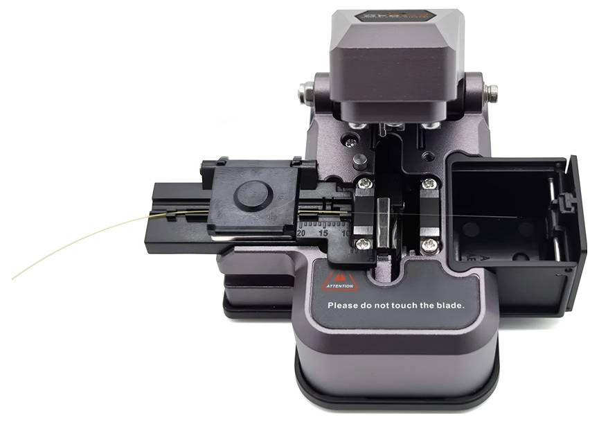Eine Kabelschneidemaschine mit einem Glasfaserkabel, das zum Schneiden positioniert ist. Ein Warnschild liest: „Bitte berühren Sie die Klinge nicht.