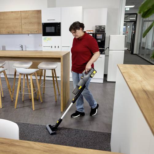 Eine Person saugt den Boden in einer modernen Küche mit Holzschränken und Hockern und sorgt für Sauberkeit in der Wohnumgebung.