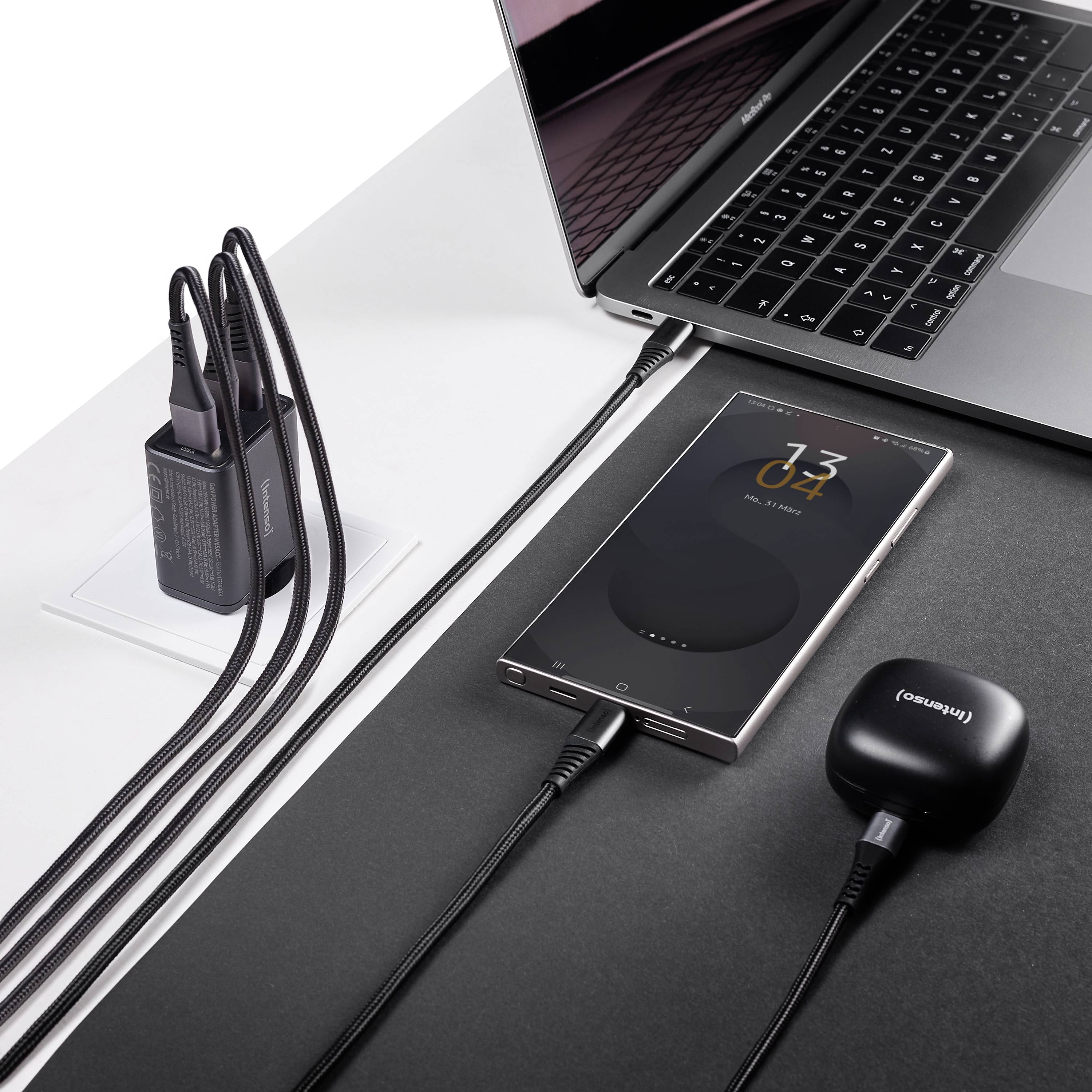 Smartphone, der auf einem Ladegerät neben einem Laptop und einem angeschlossenen Ladekabel kabellos aufgeladen wird.
