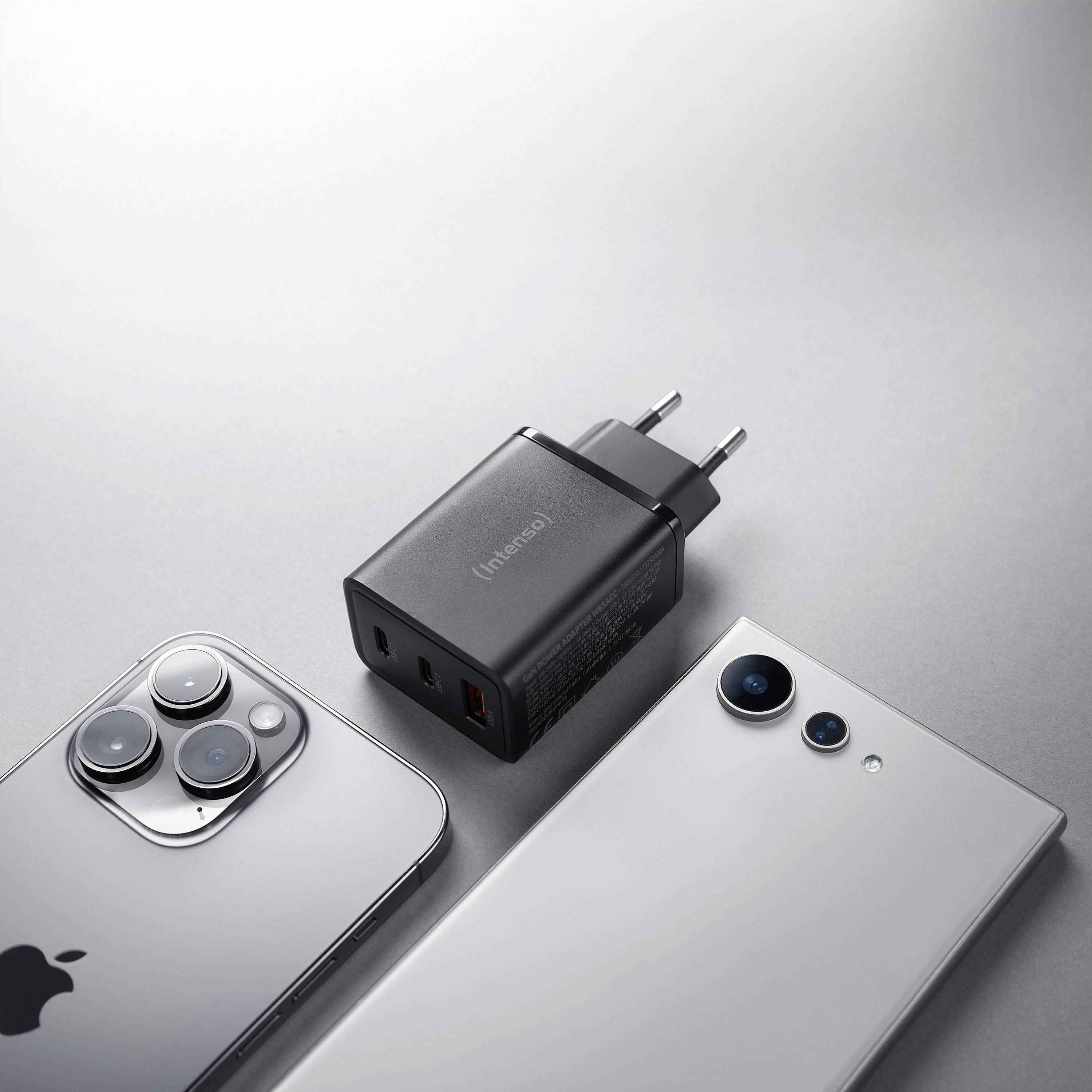 Zwei Smartphones, eines silber mit drei Kameras und eines weiß mit zwei Kameras, liegen neben einem schwarzen USB-Ladegerät mit mehreren Anschlüssen.