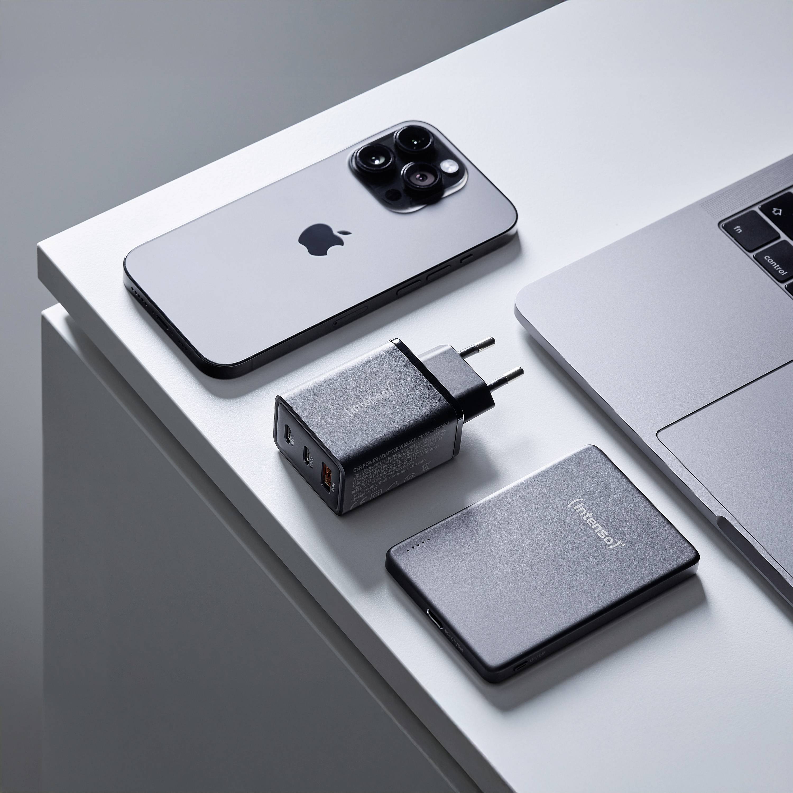 Ein Smartphone, ein Laptop, ein tragbarer Ladegerät und ein USB-Adapter sind ordentlich auf einem Tisch angeordnet und zeigen ein minimalistisches Technik-Setup.