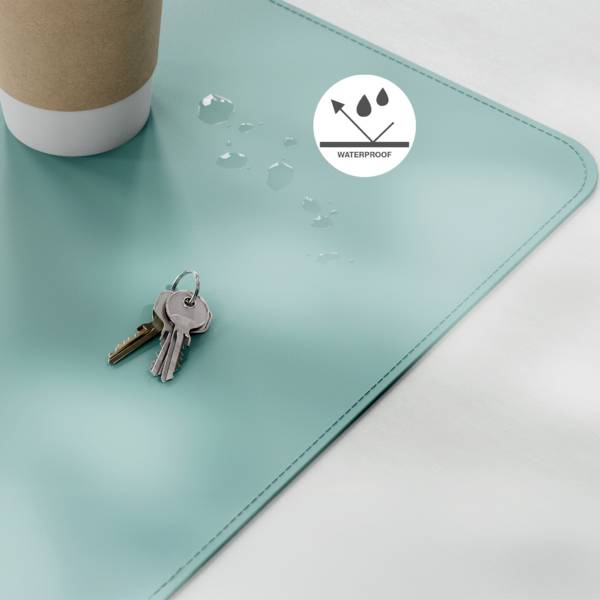 Eine Kaffeetasse und Schlüssel liegen auf einem türkisfarbenen wasserdichten Schreibtischunterlag. Wassertropfen unterstreichen die wasserdichte Eigenschaft des Unterlegs.