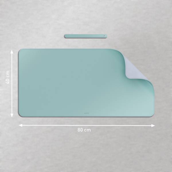 Eine petrolblaue Schreibunterlage mit den Maßen 80 cm x 40 cm, deren obere rechte Ecke leicht aufgerollt ist, liegt auf einer grauen Oberfläche.