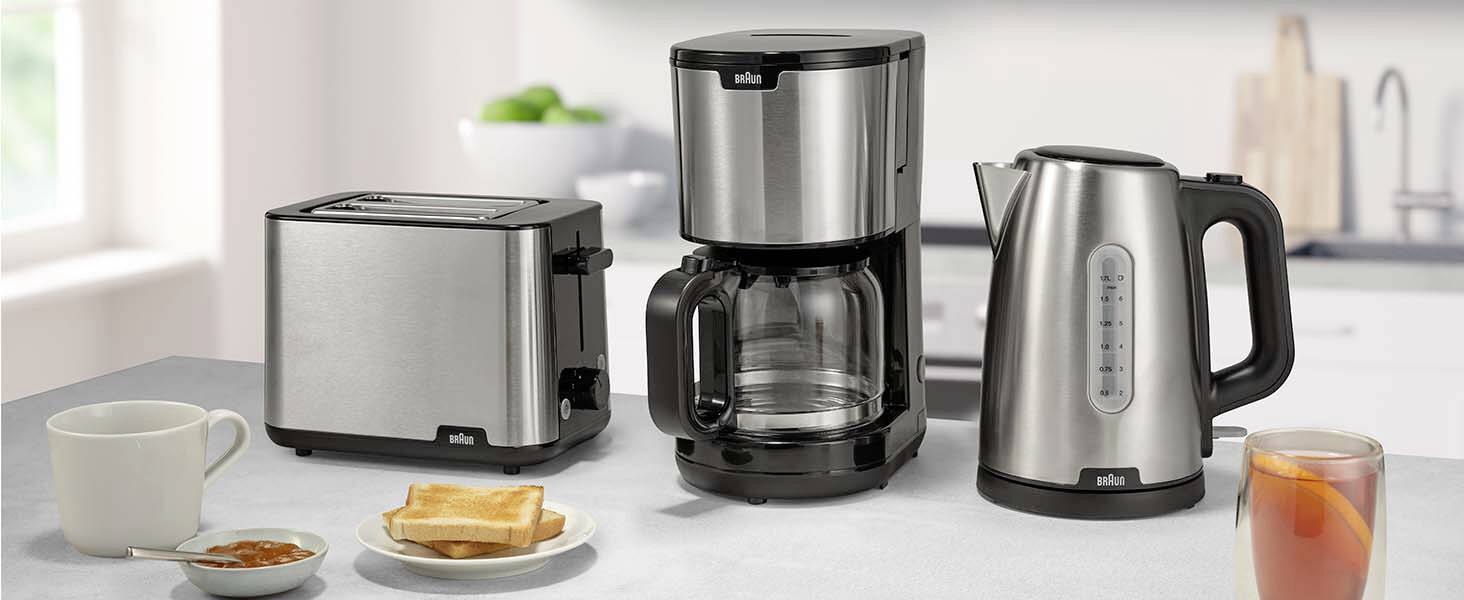 Eine Küchenarbeitsplatte zeigt einen silbernen Toaster, eine Kaffeemaschine und einen elektrischen Wasserkocher. Eine Tasse, Toast und ein Glas Saft befinden sich in der Nähe.