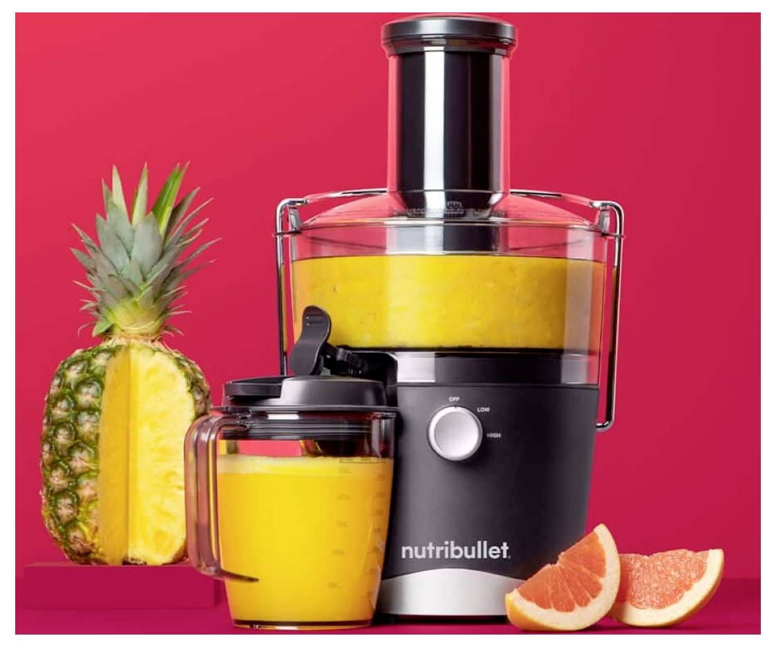 Ein schwarzer Nutribullet-Entsafter wird zusammen mit einem Behälter Orangensaft, einer halbierte Ananas und Grapefruitscheiben vor einem roten Hintergrund gezeigt.