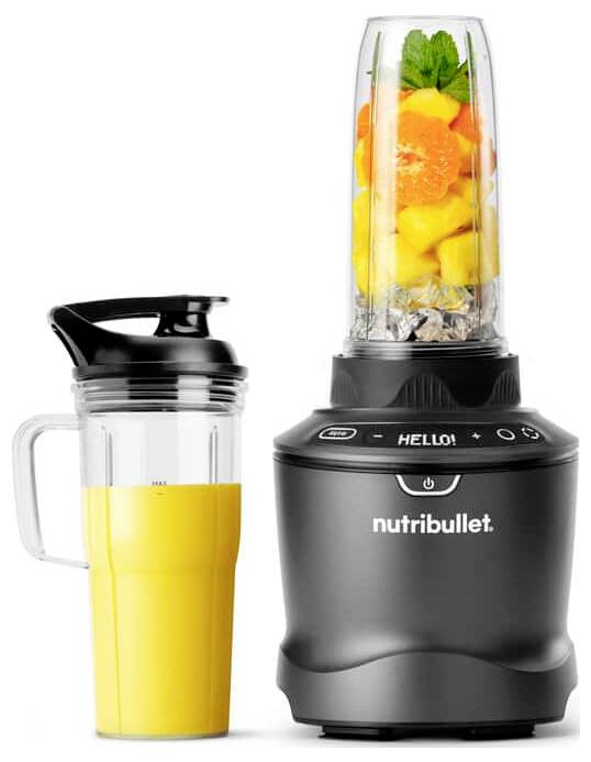 Ein Mixer mit Früchten und Nüssen steht neben einem gefüllten Reisebecher. Der digitale Bildschirm des Mixers zeigt 