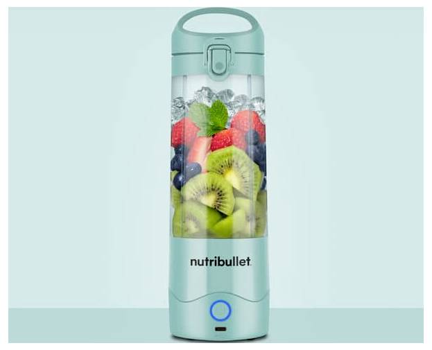 Ein türkisfarbener Nutribullet-Mixer, gefüllt mit geschnittenen Kiwis, Erdbeeren, Blaubeeren und Minzblättern, vor einem hellblauen Hintergrund.