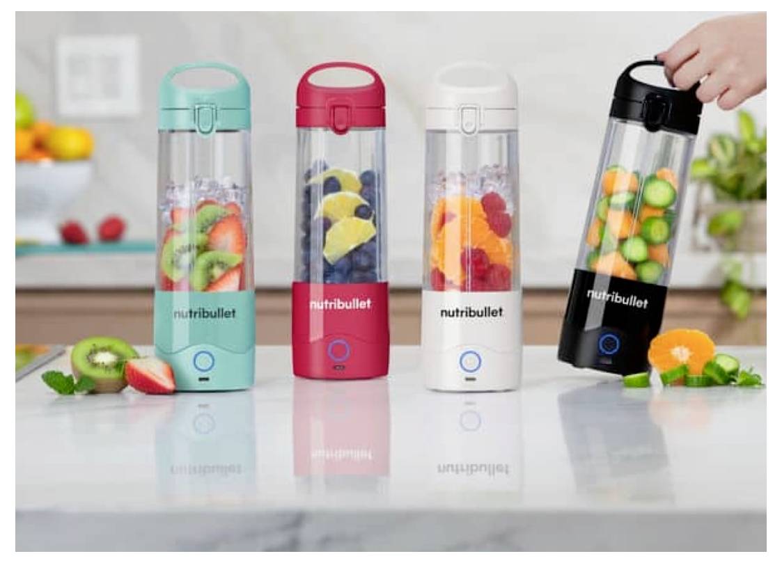 Vier Nutribullet-Mixer in den Farben Petrol, Rot, Weiß und Schwarz, jeweils gefüllt mit verschiedenen Früchten, sind auf einer Küchenarbeitsplatte platziert.