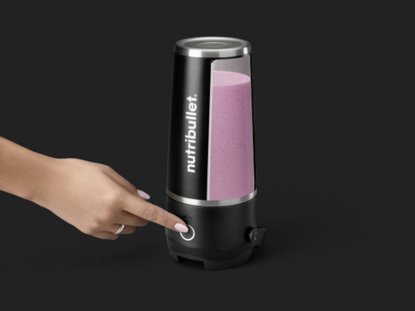 Eine Hand einer Person drückt den Knopf eines Nutribullet-Standmixers, der einen pinken Smoothie enthält, vor einem schwarzen Hintergrund.