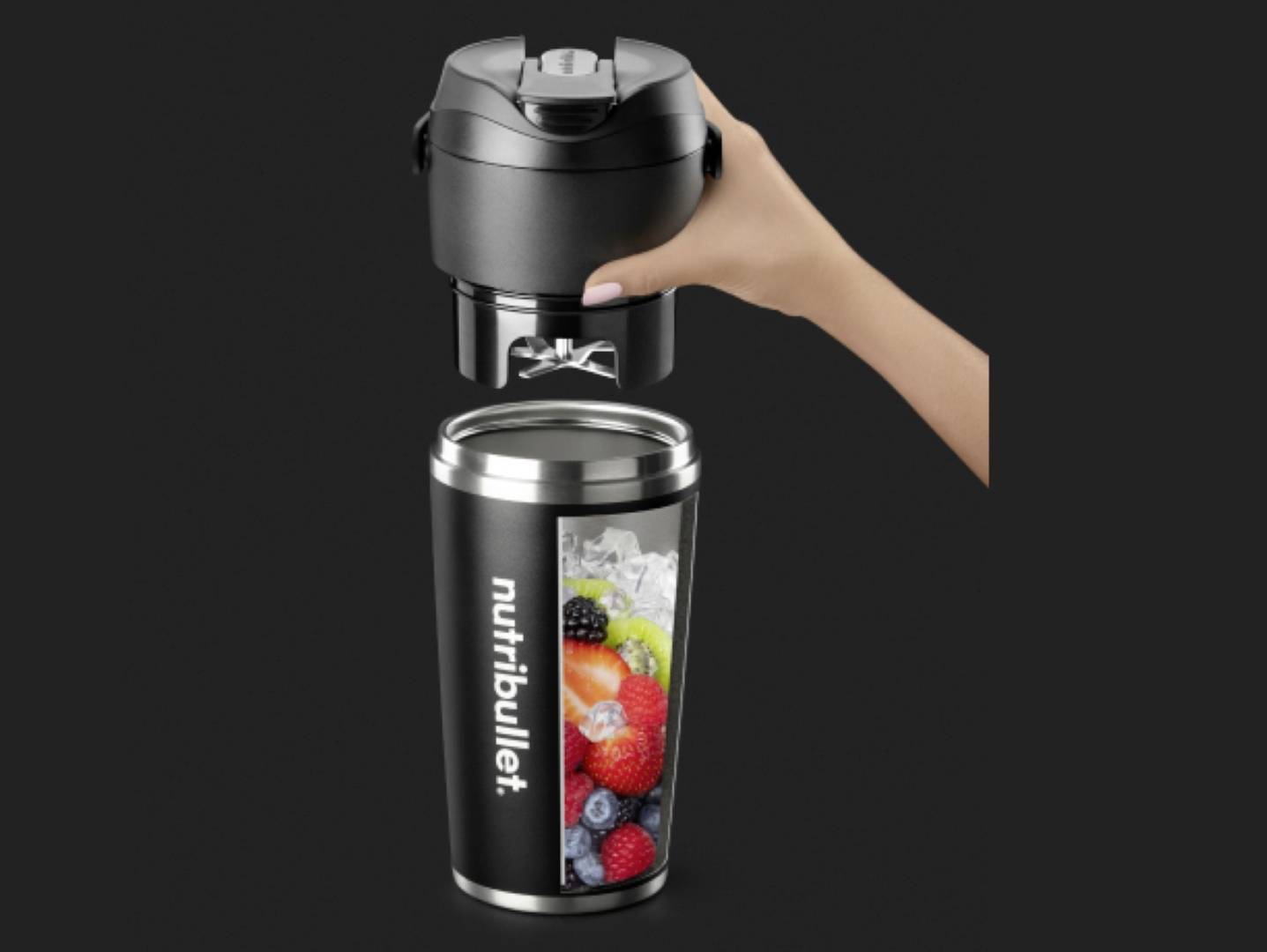 Eine schwarze NutriBullet-Blenderkanne, gefüllt mit Eis und verschiedenen Früchten, wird von einer Hand auf ihre schwarze motorisierte Basis gestellt.