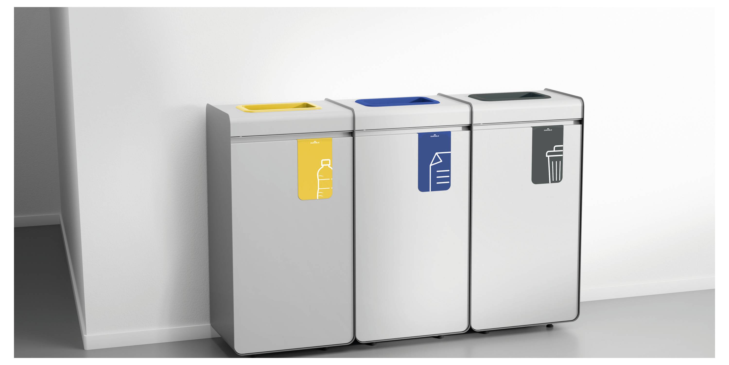 Drei Recyclingbehälter an einer Wand mit Beschriftungen: gelb für Plastik, blau für Papier und grau für Restmüll.