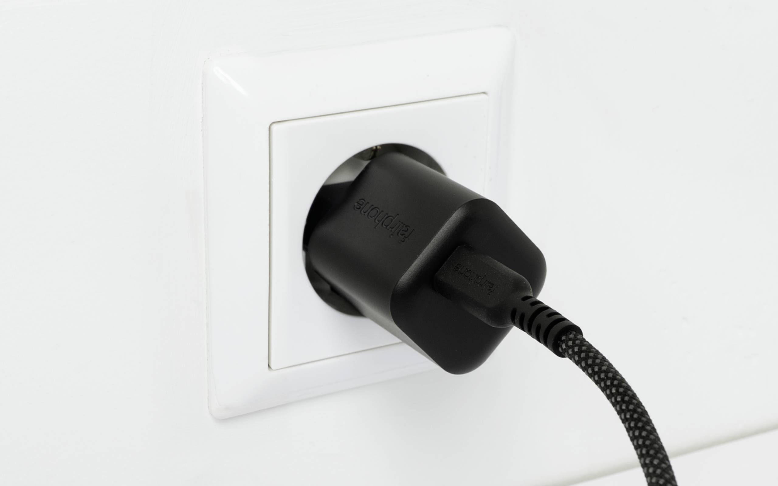 Ein schwarzes Netzteil, das in eine weiße Wandsteckdose eingesteckt ist.