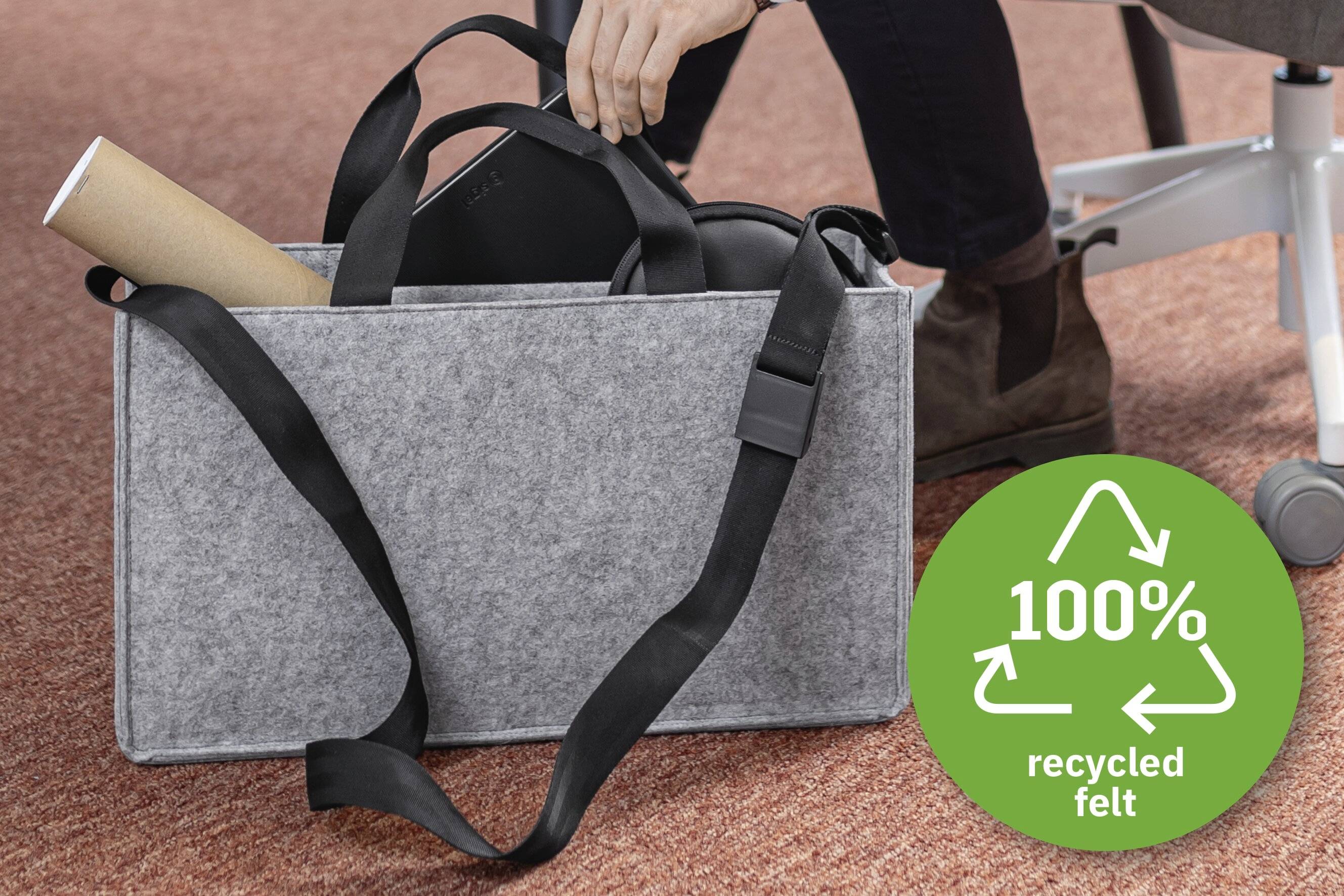 Eine graue Filztasche mit schwarzen Riemen enthält eine aufgerollte Poster und ein Gerät. Ein grüner Ausweis weist '100% recycelten Filz' aus.
