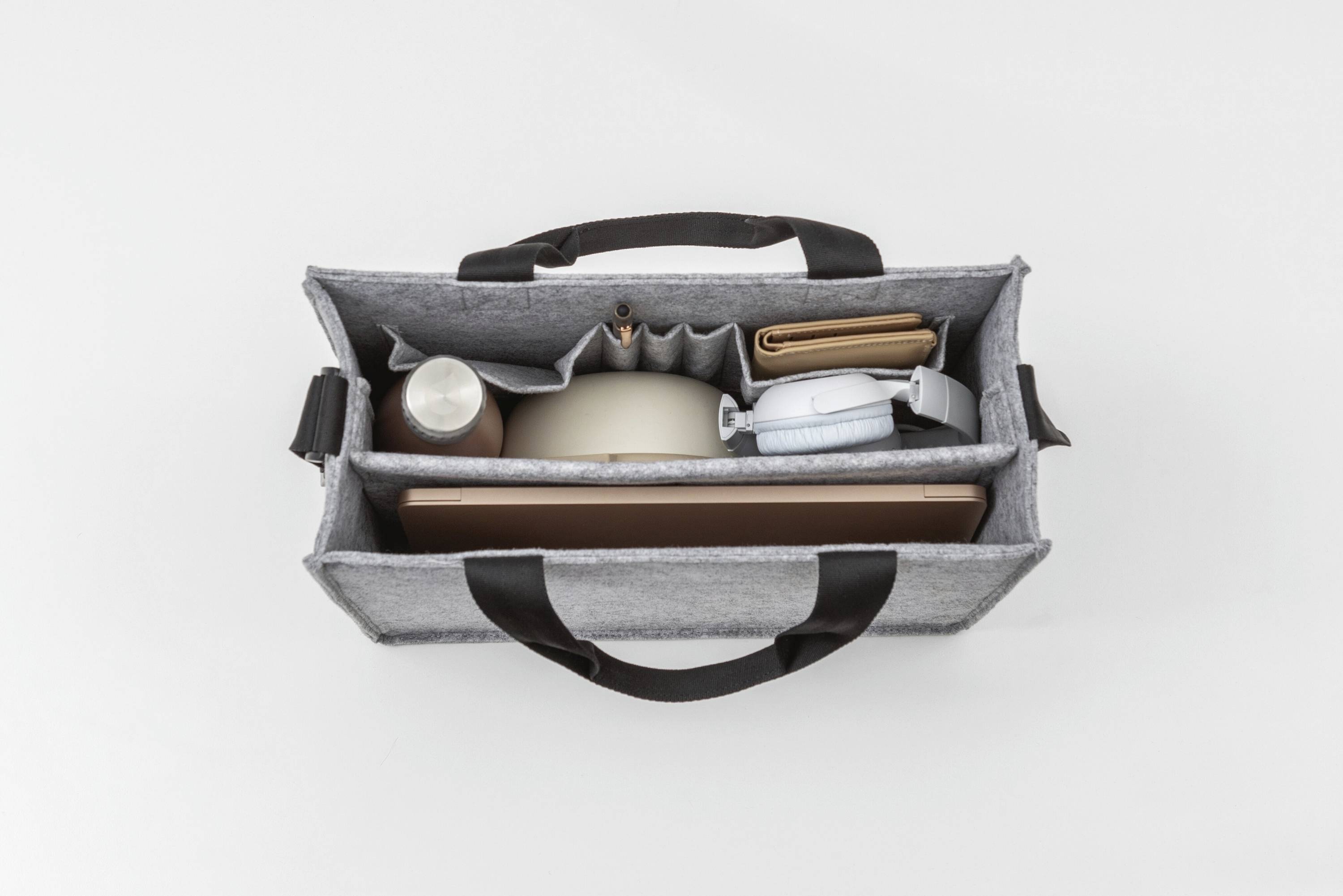 Eine Draufsicht einer geöffneten grauen Filztasche, die einen Laptop, eine Wasserflasche, ein Portemonnaie und einige kleine Gegenstände enthält, die in Taschen organisiert sind.