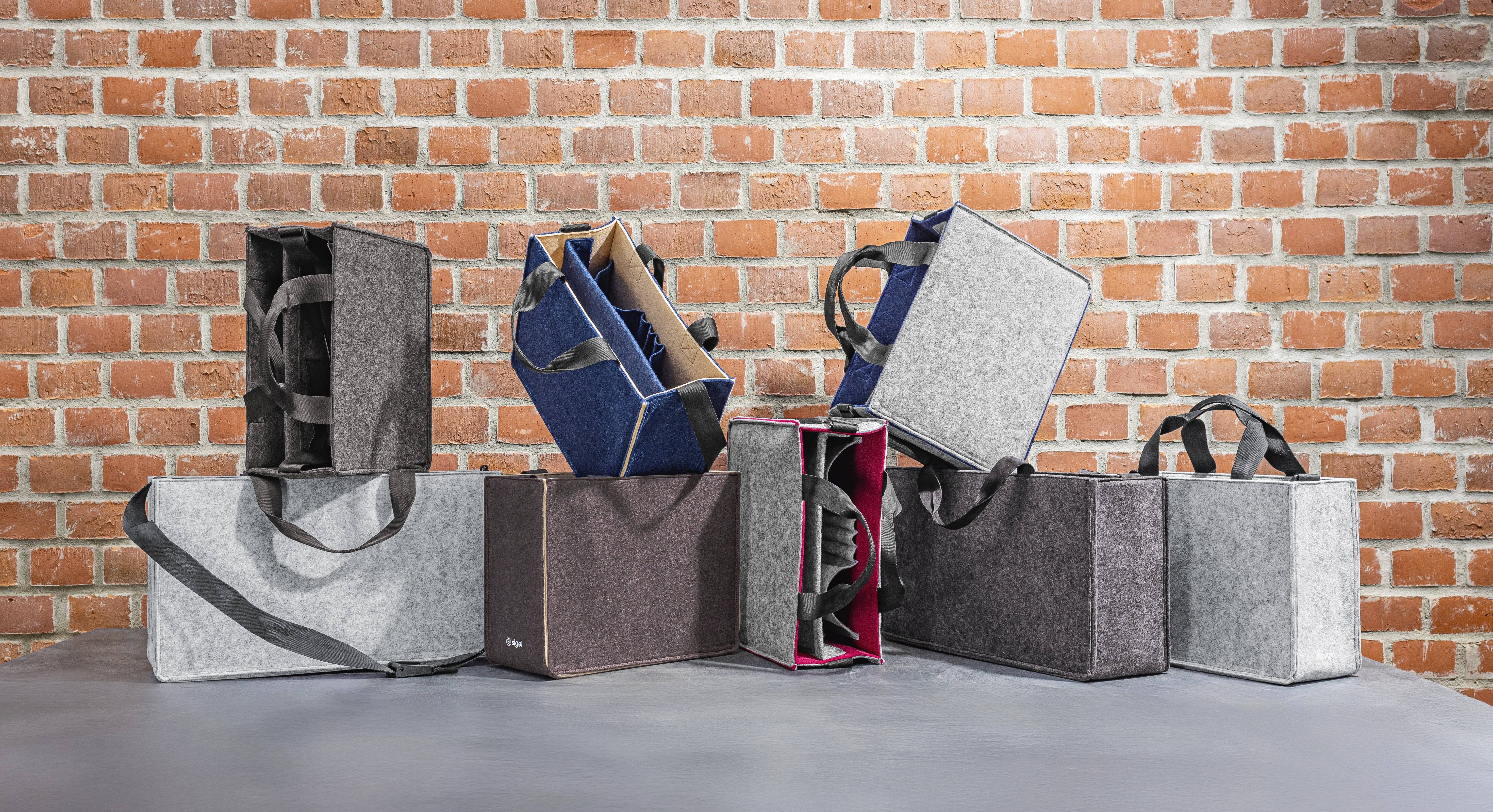 Einkaufstaschen in verschiedenen Farben und Materialien, die auf einer grauen Oberfläche vor einer Ziegelwand angeordnet sind.