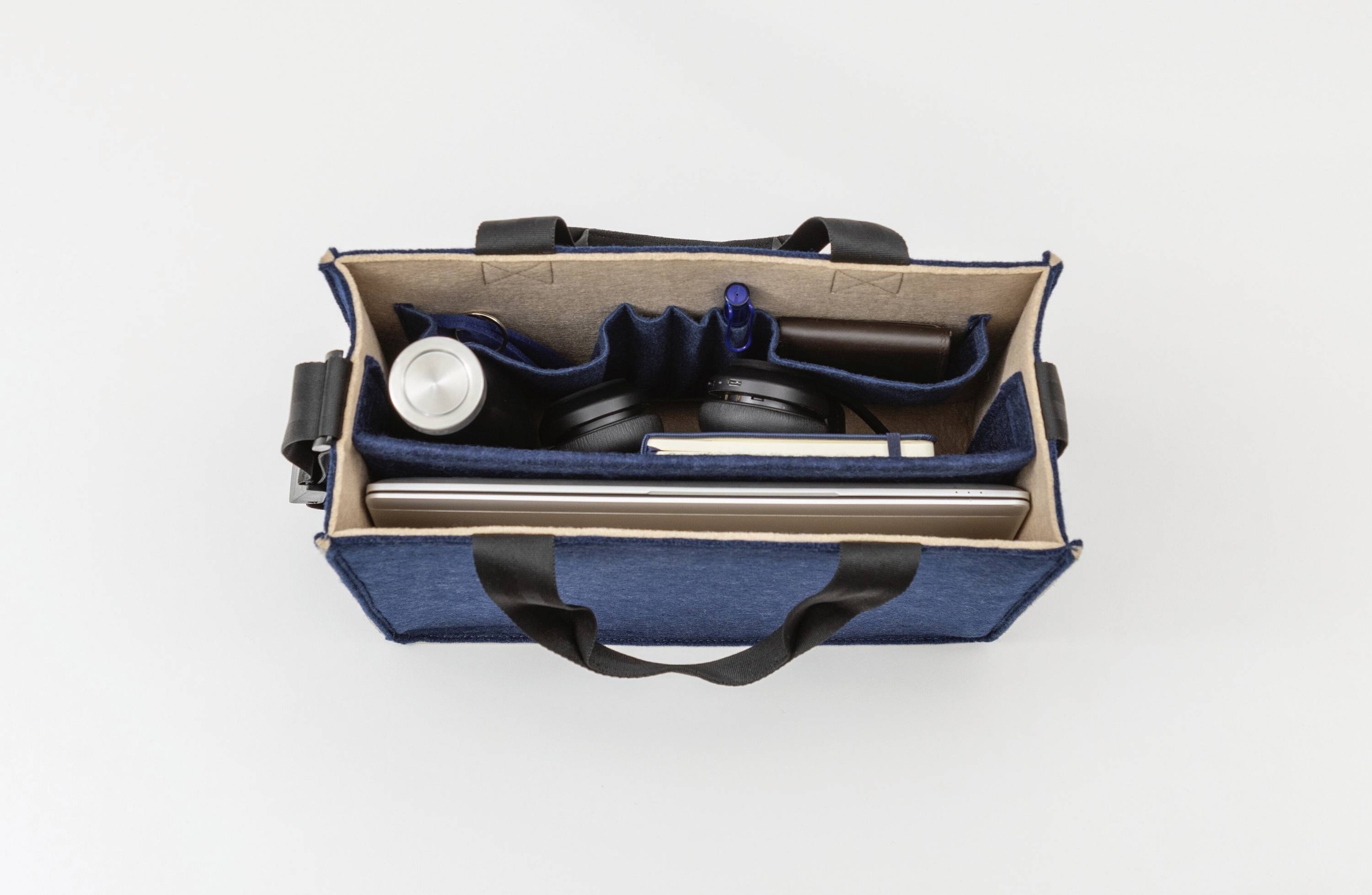 Offene blaue Tasche, von oben betrachtet, mit einer Wasserflasche, Kopfhörern, einem Stift und einem geschlossenen Laptop, die ordentlich in Fächern angeordnet sind.