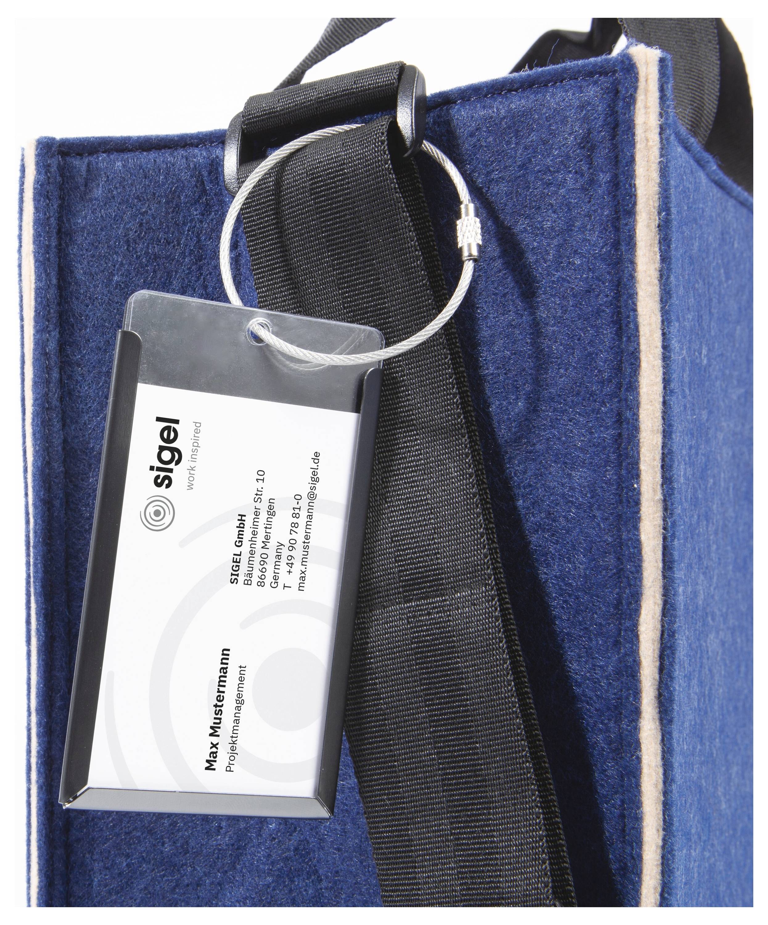 Ein Namensschild mit 'Max Westermann' und Firmendetails hängt mittels einer Metallschlaufe an einem blauen Stoffbeutel.