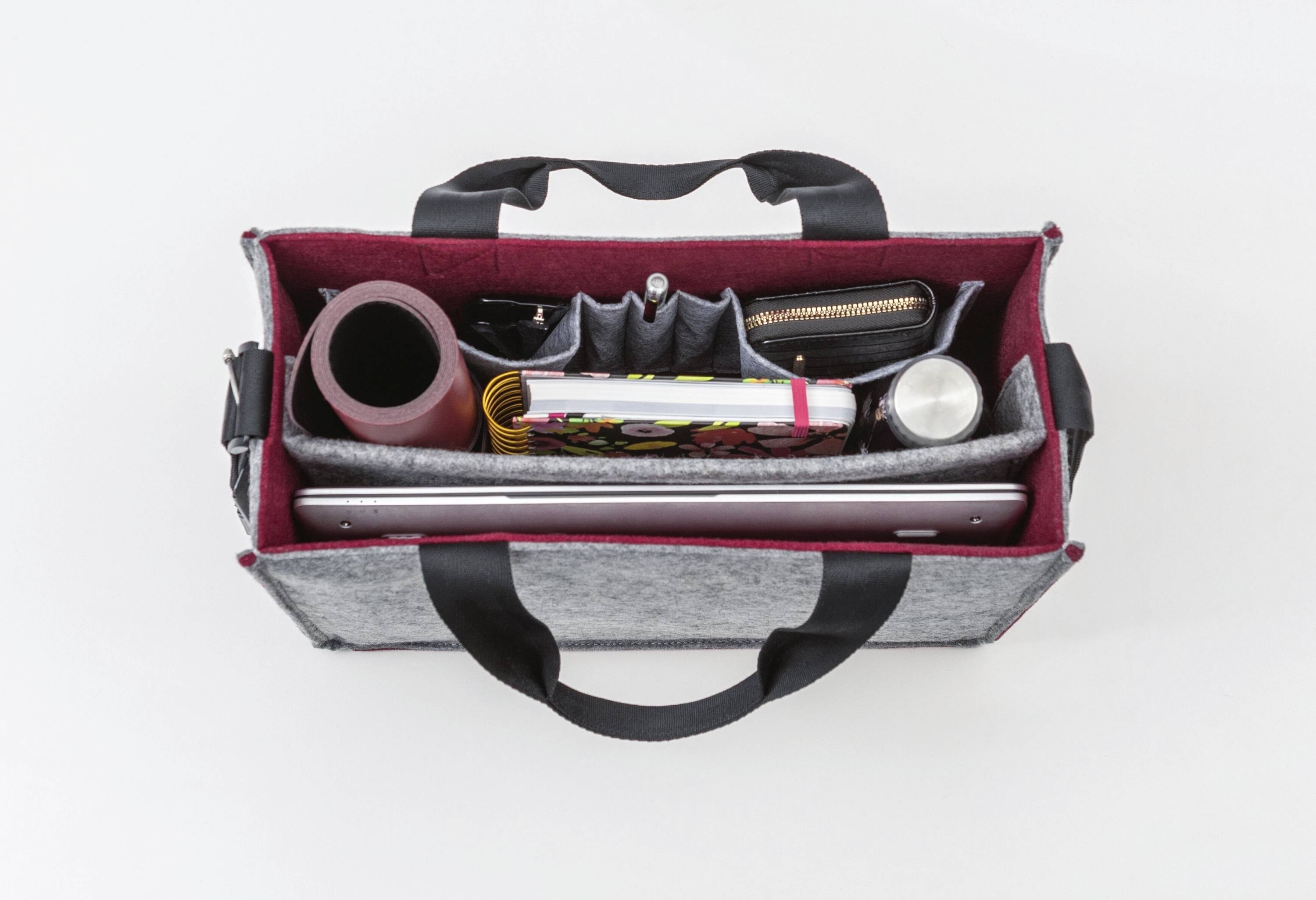 Draufsicht einer geöffneten Organizertasche mit Fächern, die einen Laptop, eine Wasserflasche, eine zusammengerollte Matte, eine bunte Tasche und andere Gegenstände beinhalten.
