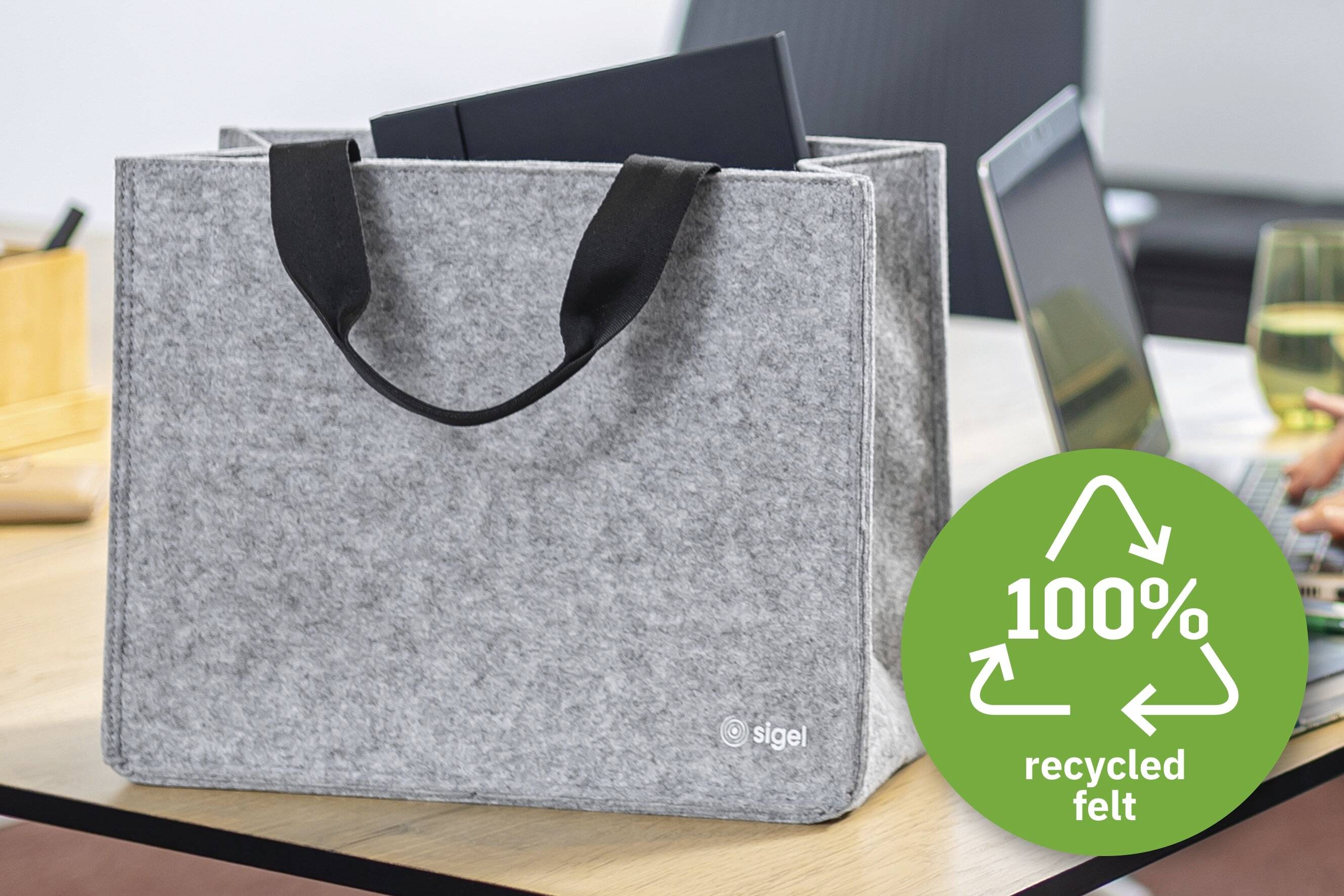 Eine graue Filz-Tragetasche mit schwarzen Griffen auf einem Tisch, mit der Aufschrift 