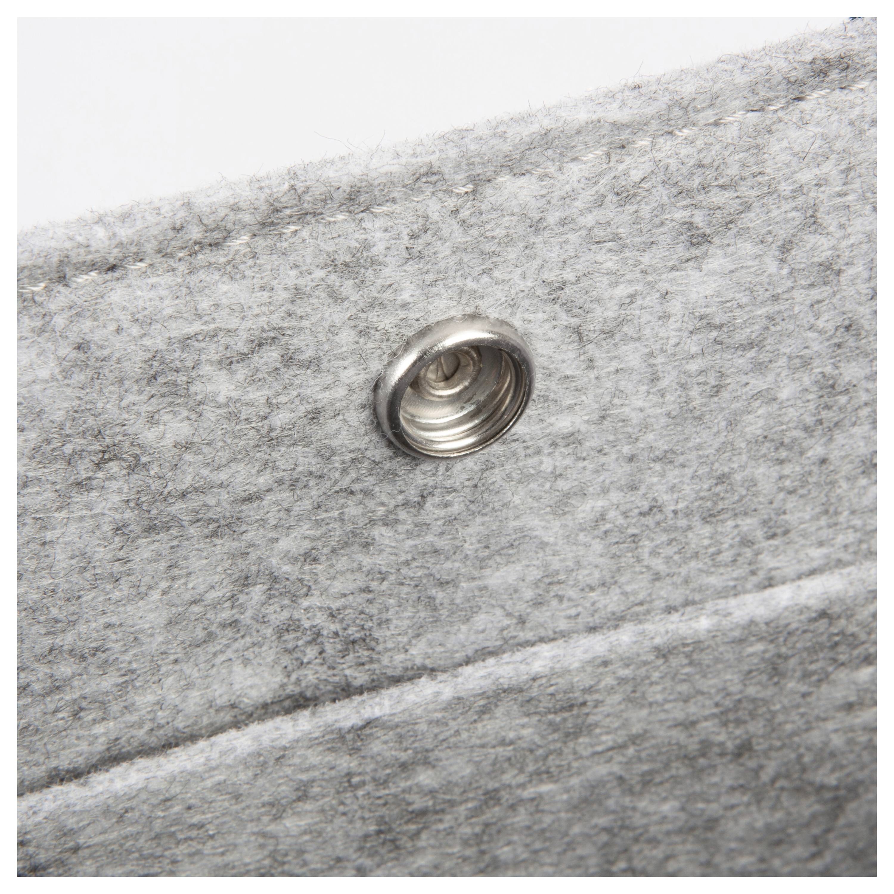 Nahaufnahme einer Metalldruckknopfes auf grauem Filzstoff, mit Fokus auf die Textur und Positionierung des Knopfes auf dem Material.