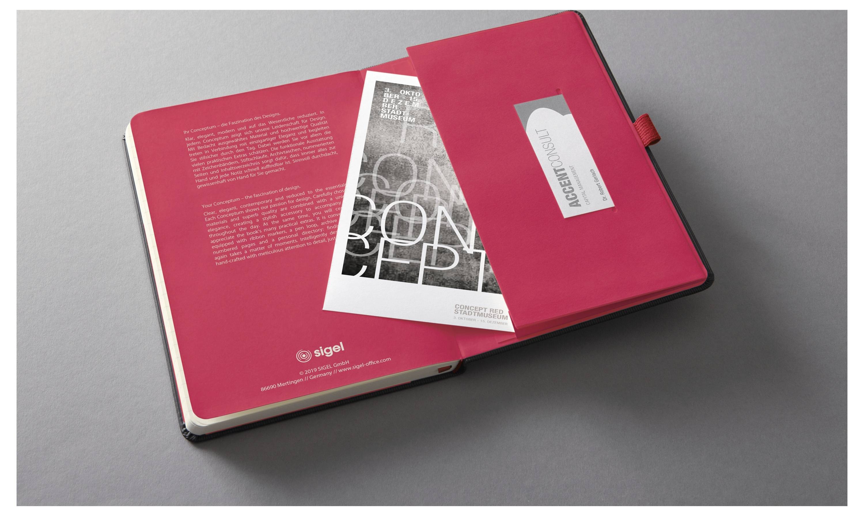 Öffne rotes Notizbuch mit einer Innentasche, in der eine schwarz-weiße Karte und eine Visitenkarte stecken. Auf der linken Seite befindet sich eine Seite mit gedrucktem Text.