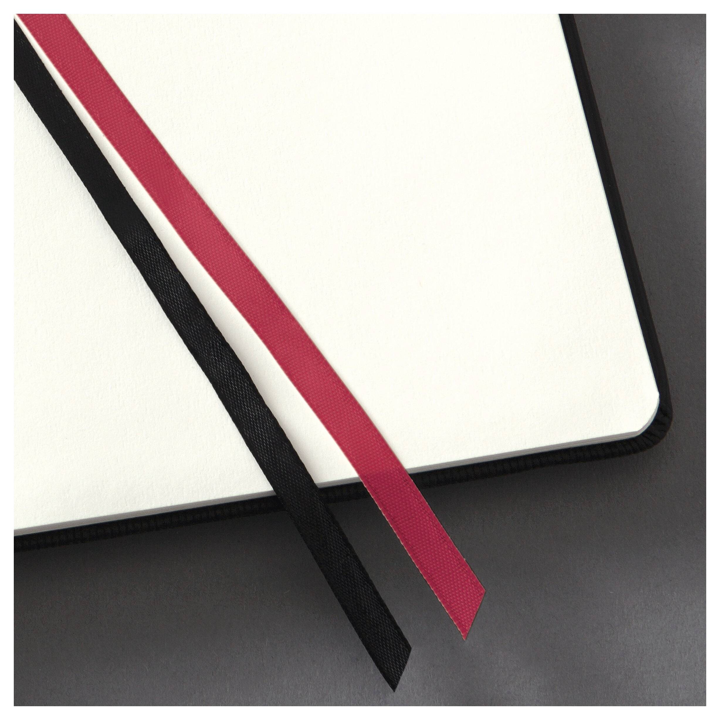 Ein offenes Notizbuch mit schwarzem Einband liegt auf einer dunklen Oberfläche. Zwei Buchbänder, eines in Rot und eines in Schwarz, ragen aus den Seiten hervor.