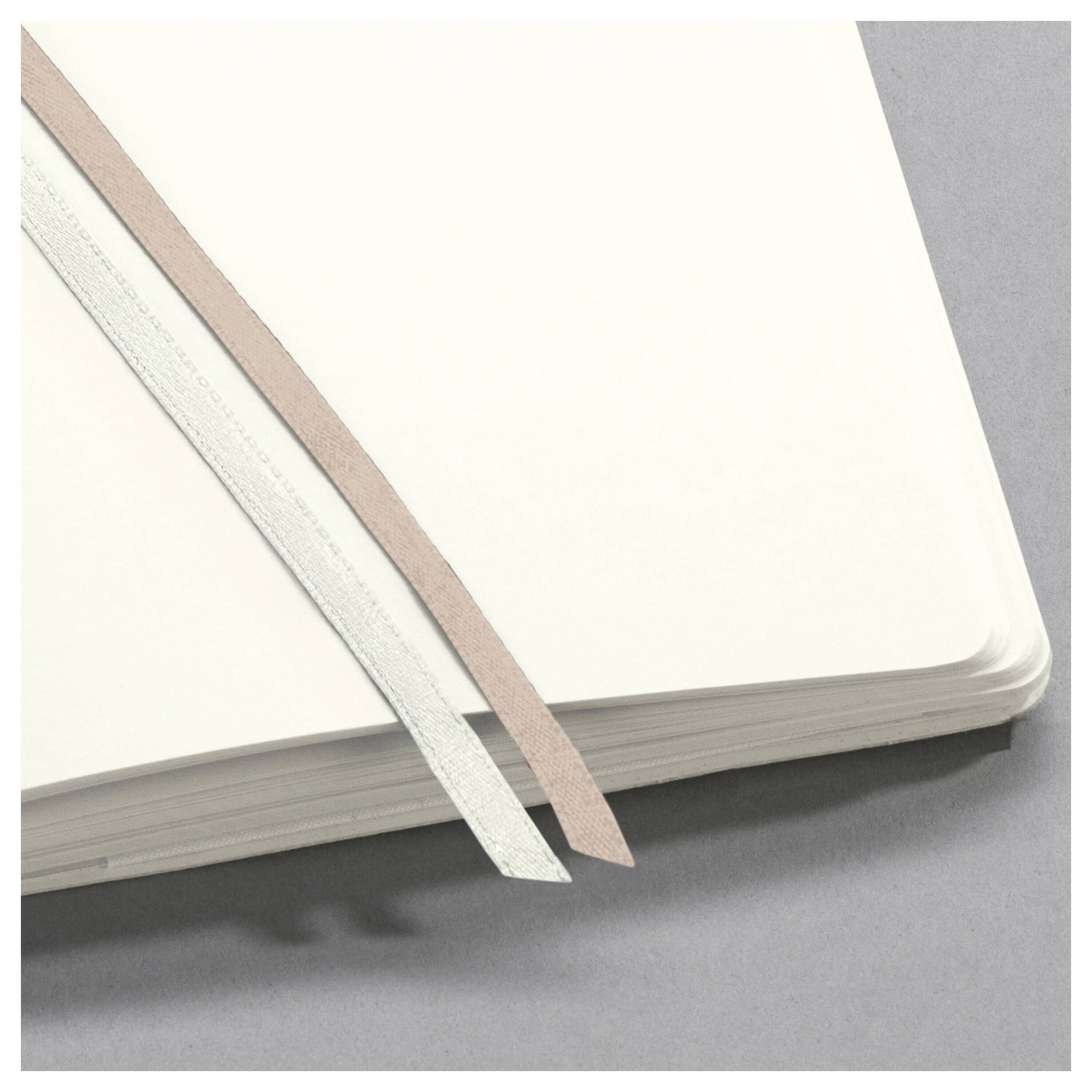 Ein offenes Notizbuch mit einem hellrosa und einem weißen Lesezeichen auf einer grauen Oberfläche.