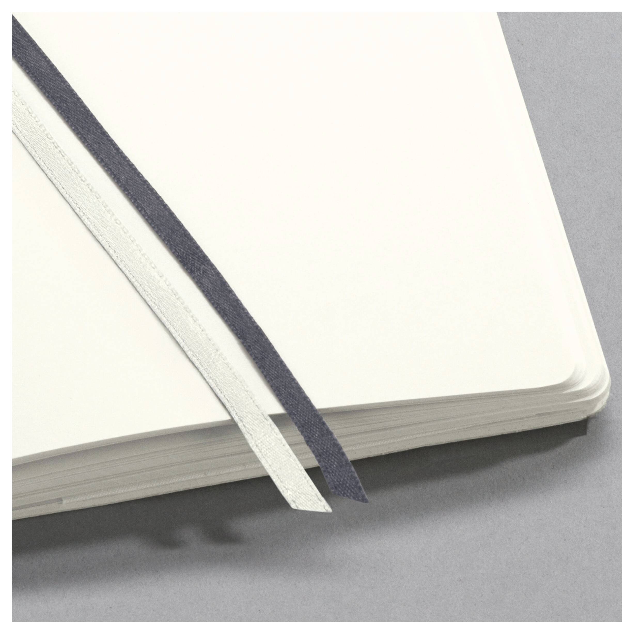 Offenes Notizbuch mit leeren Seiten und zwei diagonal platzierten Buchbändern, eines weiß und eines schwarz, auf einem grauen Hintergrund.