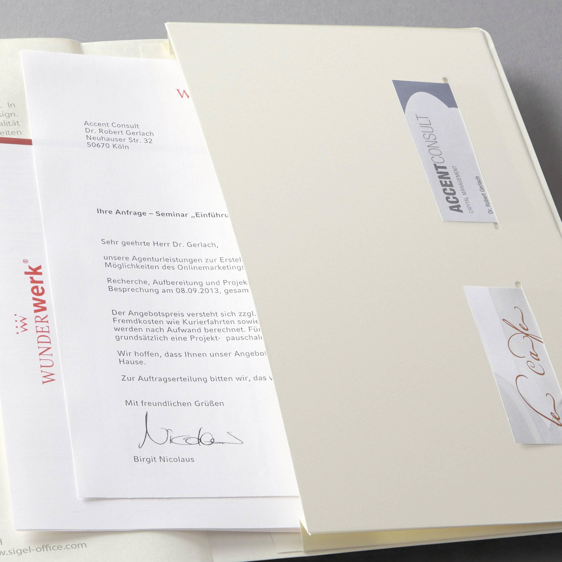 Ein Stapel von Dokumenten, einschließlich eines Briefes, adressiert an 'Sehr geehrter Herr Dr. Gerlach', mit Visitenkarten von WUNDERWERK und ACCENT CONSULT.