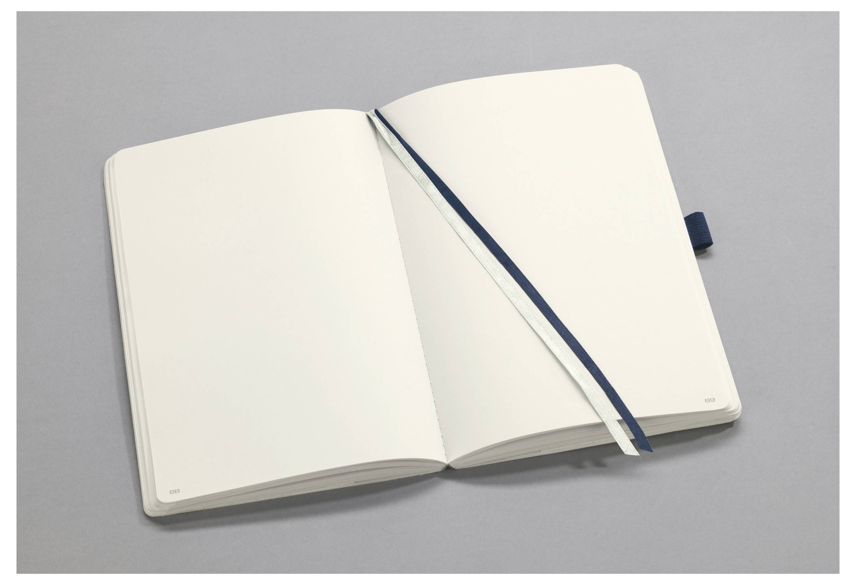 Offenes leeres Notizbuch mit blauem Lesebändchen auf einer grauen Oberfläche.