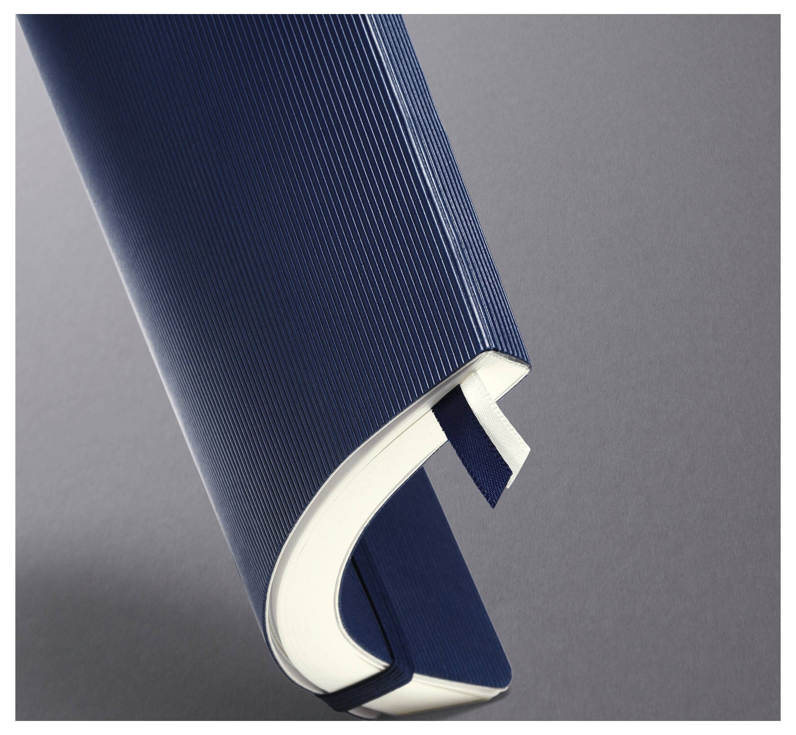 Eine Nahaufnahme eines blauen Hardcover-Buches mit einer strukturierten Buchrückenseite, halb geöffnet, wobei weiße Seiten vor einem grauen Hintergrund sichtbar sind.