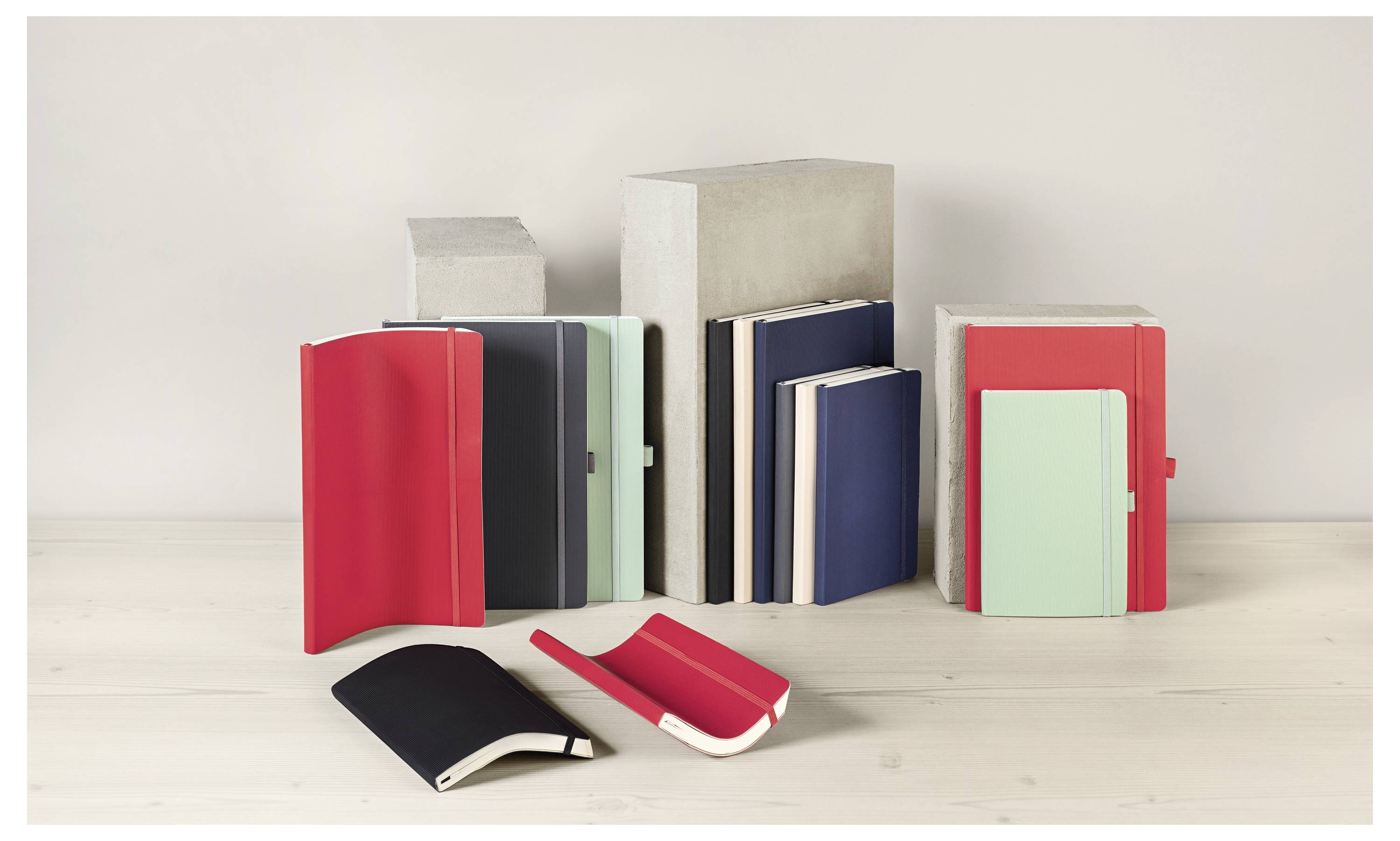 Verschiedene Notizbücher mit bunten Einbänden werden aufrecht und flach auf einer hellen Holzoberfläche präsentiert, vor einem neutralen Hintergrund.