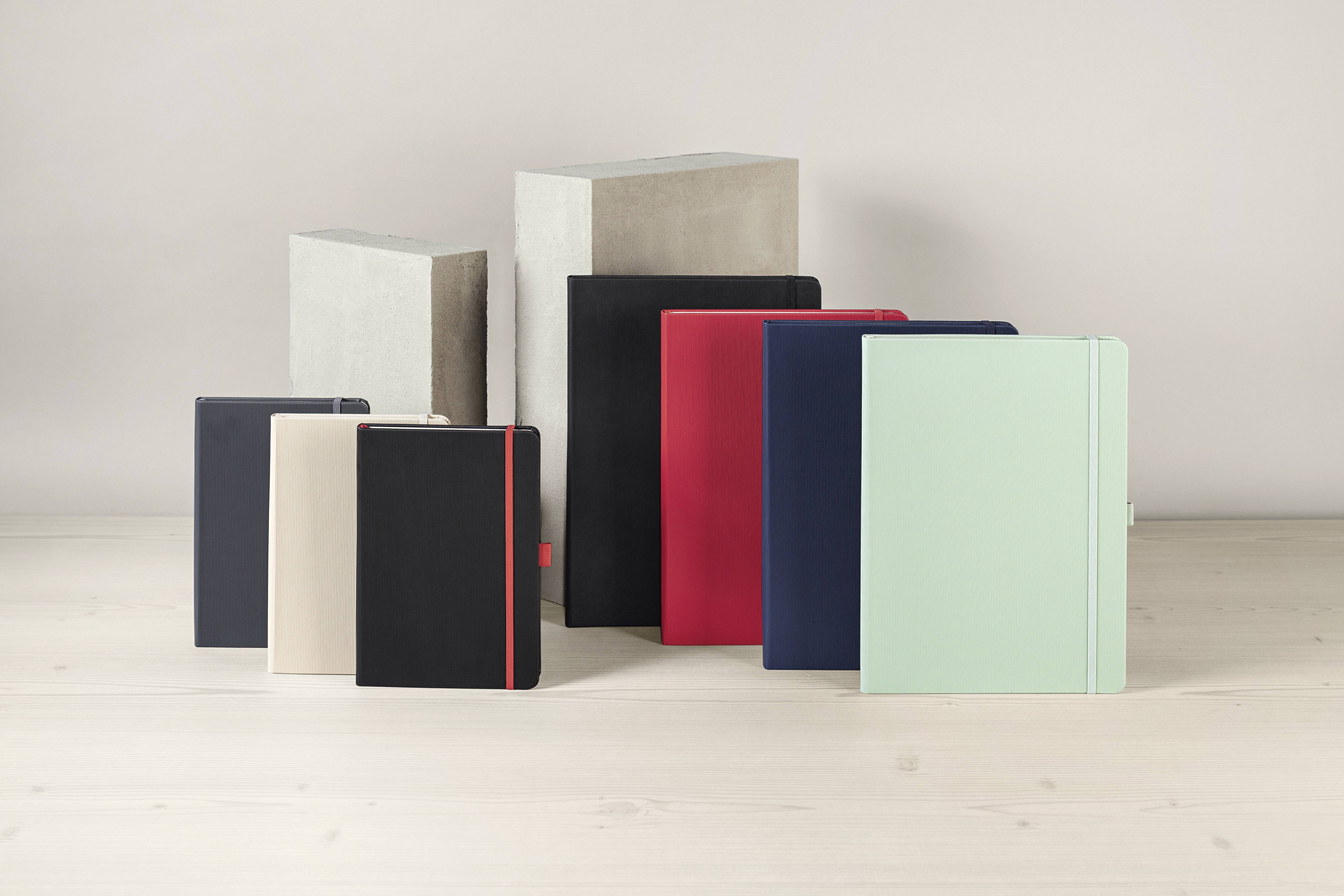 Eine Auswahl an Notizbüchern in verschiedenen Größen und Farben, darunter Schwarz, Rot und Mintgrün, die auf einer hellen Holzoberfläche ausgelegt sind.