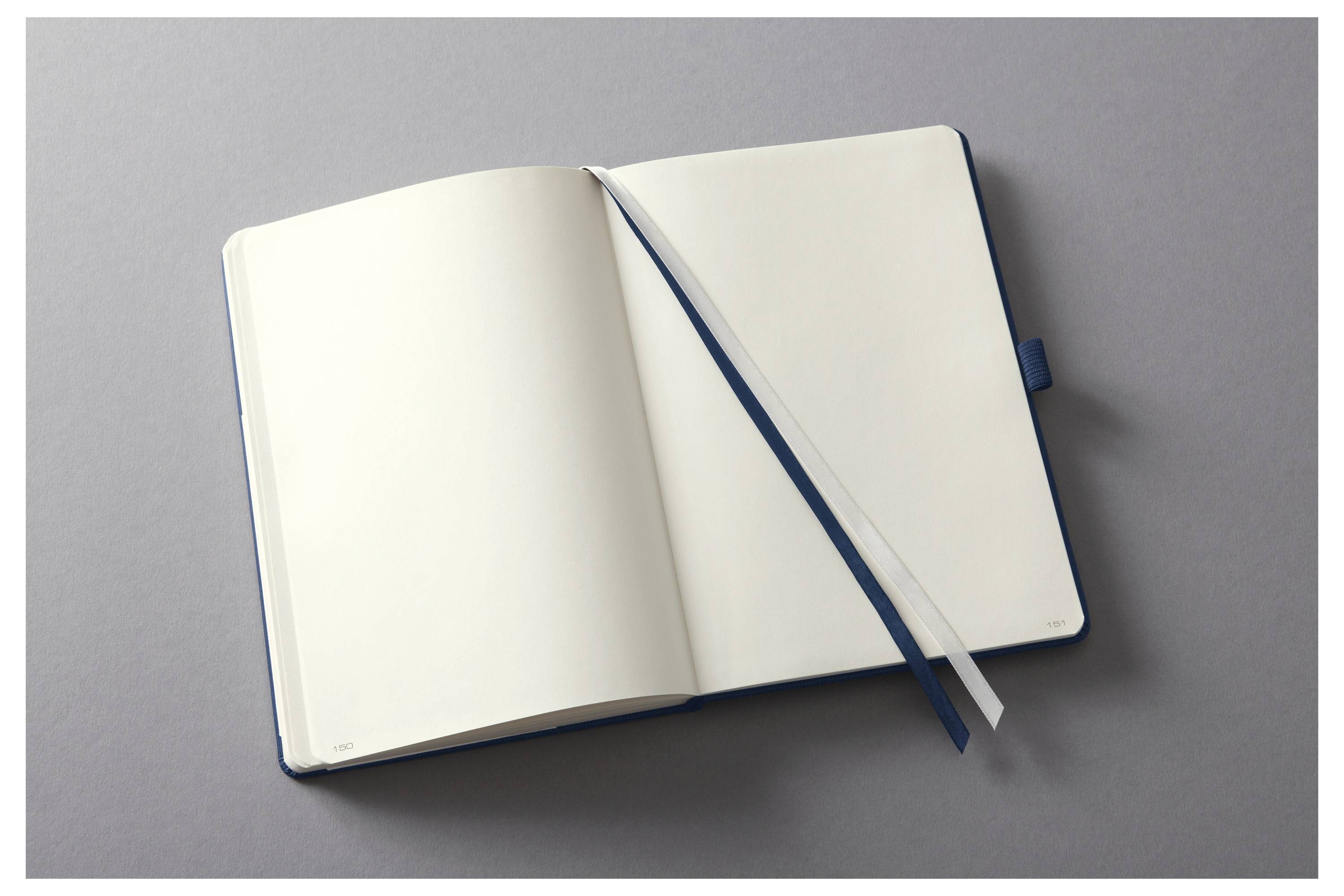 Ein offenes Notizbuch mit leeren weißen Seiten und einem weißen Lesezeichen-Band liegt auf einer grauen Oberfläche, bereit zum Schreiben oder Zeichnen.