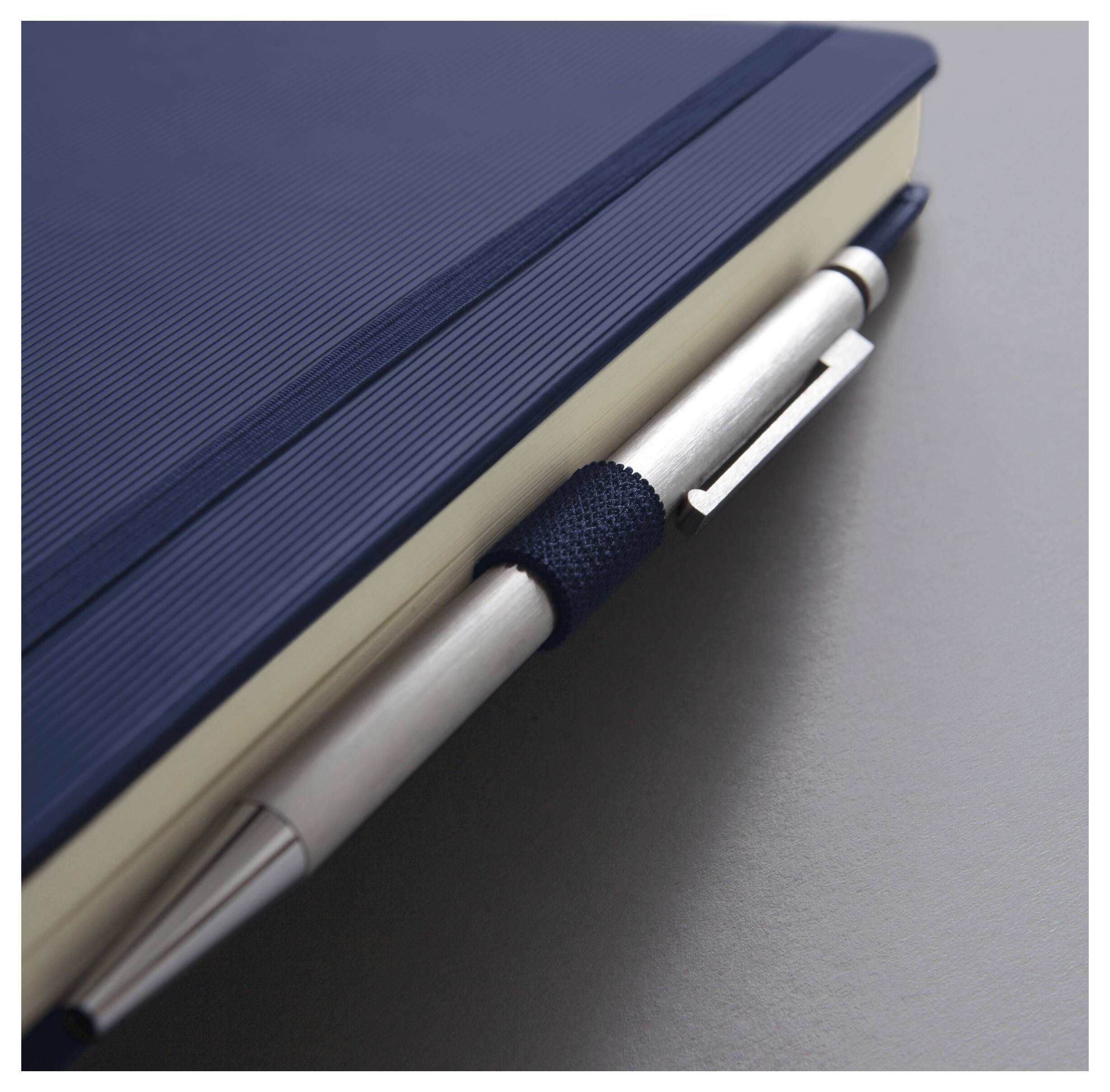 Ein marineblauer Notizblock mit einem silbernen Stift, der daran geklippt ist und auf einer grauen Oberfläche liegt.