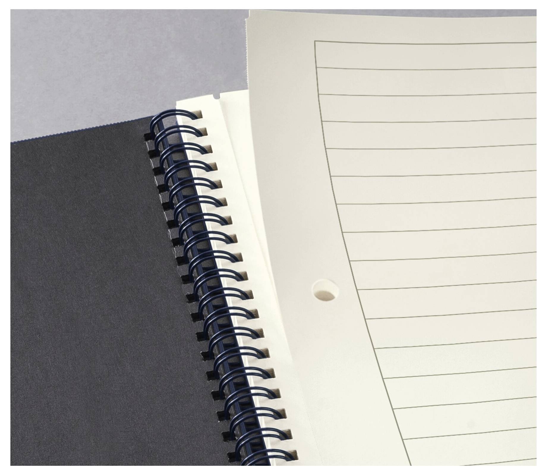 Eine Nahaufnahme eines geöffneten, spiralgebundenen Notizbuchs mit liniertem Papier, die einen Teil des schwarzen Einbands und weiße Blätter mit Lochung zeigt.
