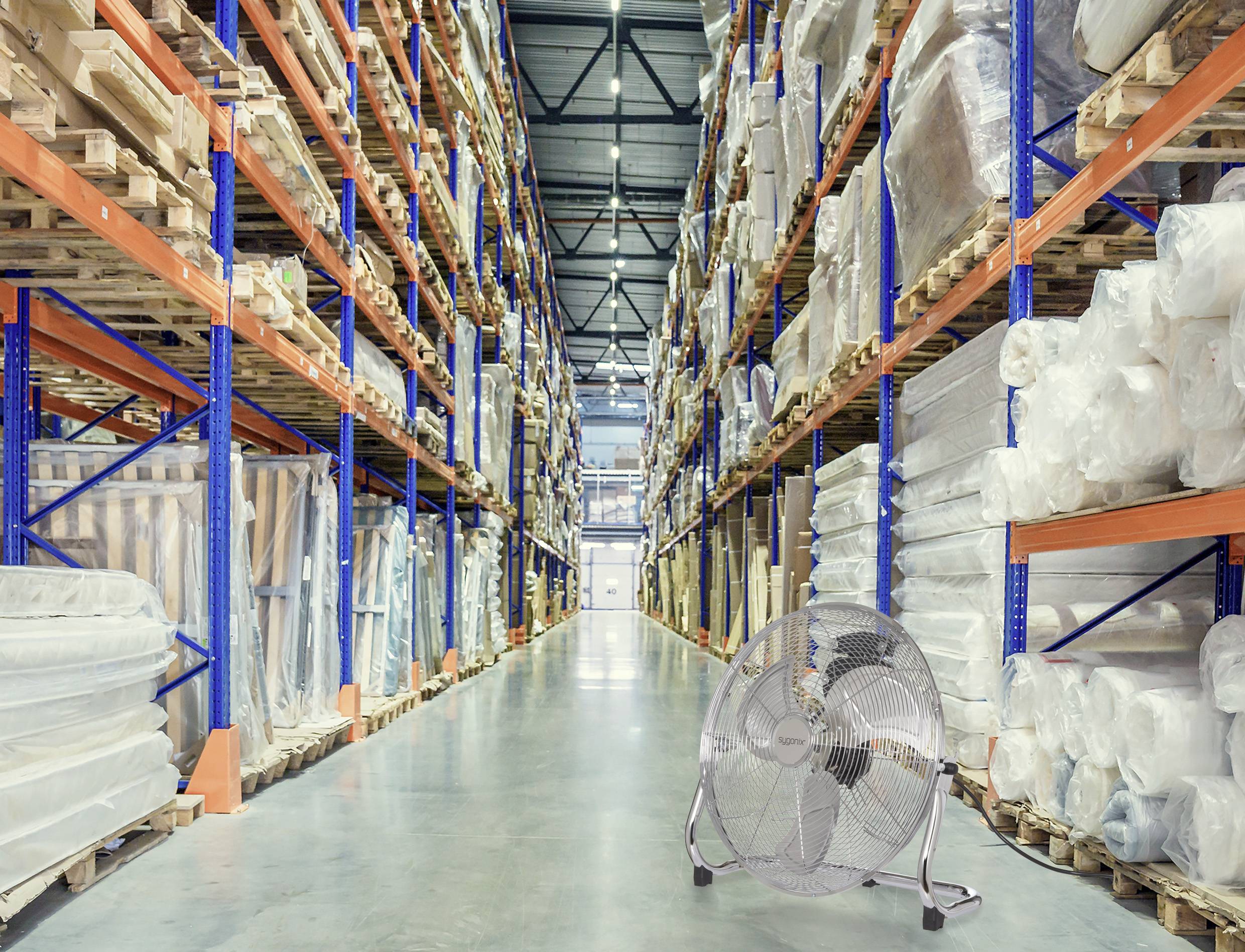 Ein großes Industrielager mit hohen Regalen, die mit eingewickelten Produkten bestückt sind. Ein großer Metalllüfter steht im Vordergrund auf dem Boden.