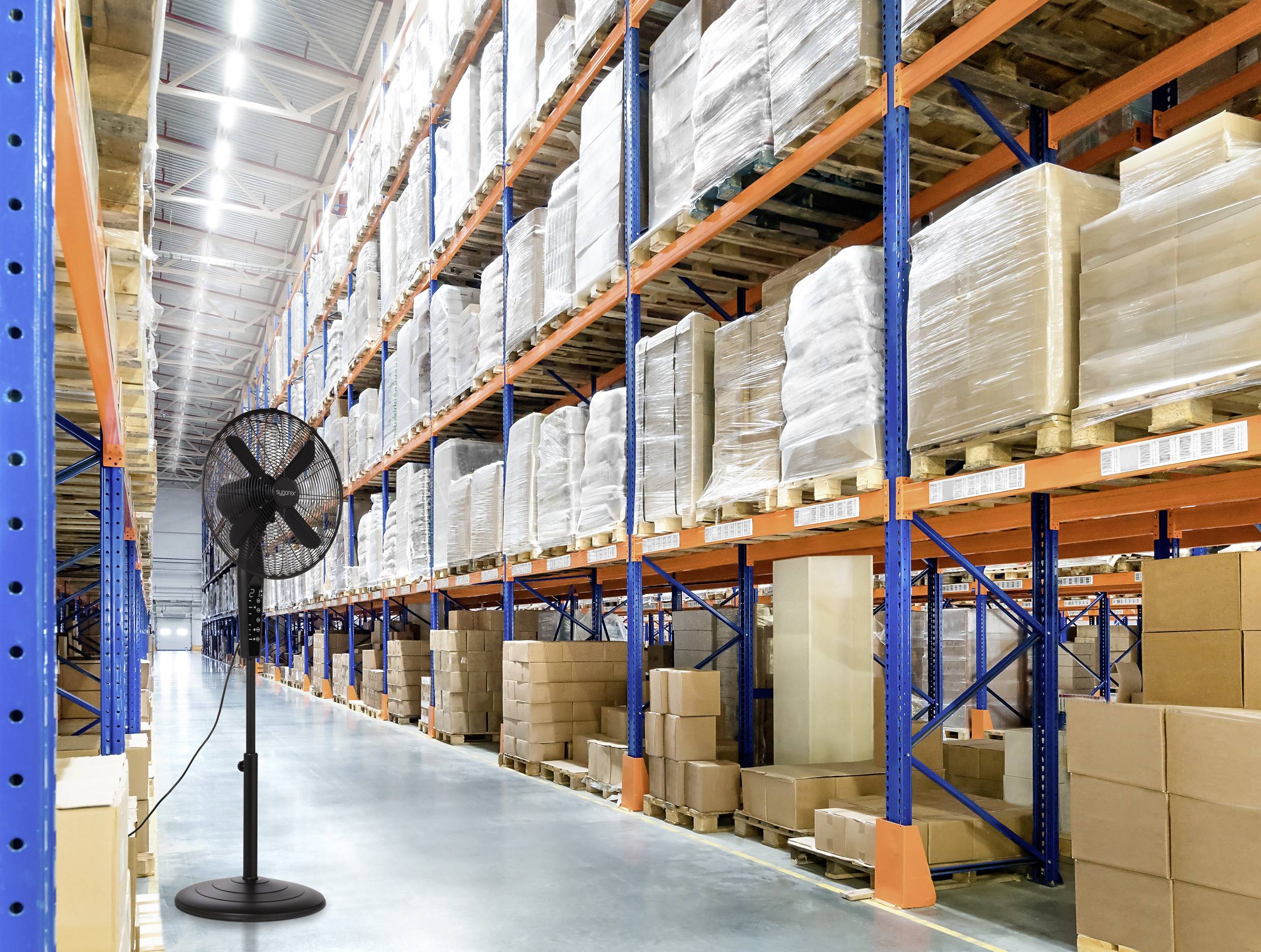 Ein großes Lagerhaus mit hohen, bestückten Regalen, die Kisten mit Waren enthalten. Ein Standventilator steht auf dem polierten Betonboden im Vordergrund.