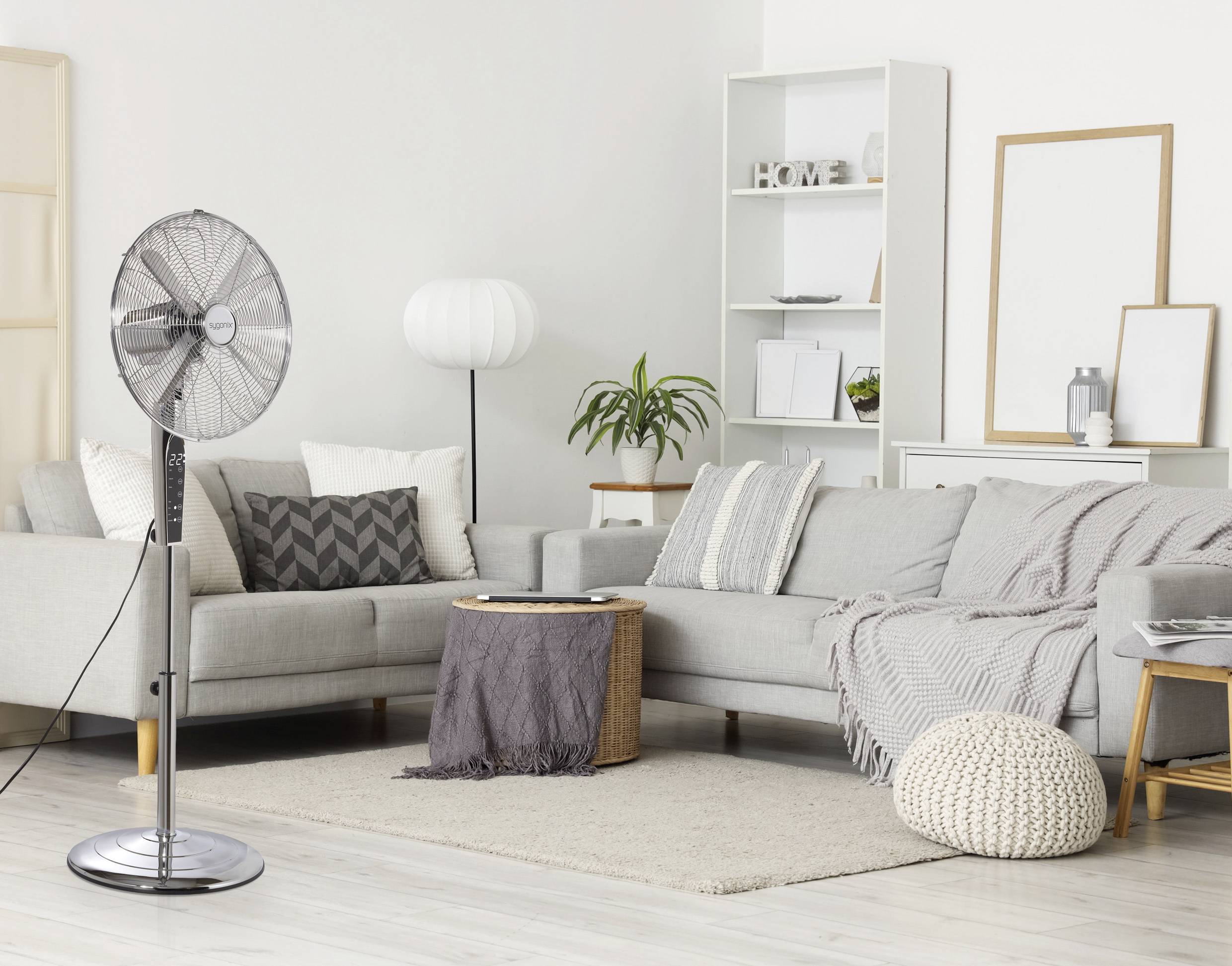 Ein modernes Wohnzimmer mit einem Standventilator, grauem Sofa, weißer Lampe und gemusterten Kissen. Ein gemütlicher, neutral getönter Raum mit einem Teppich.