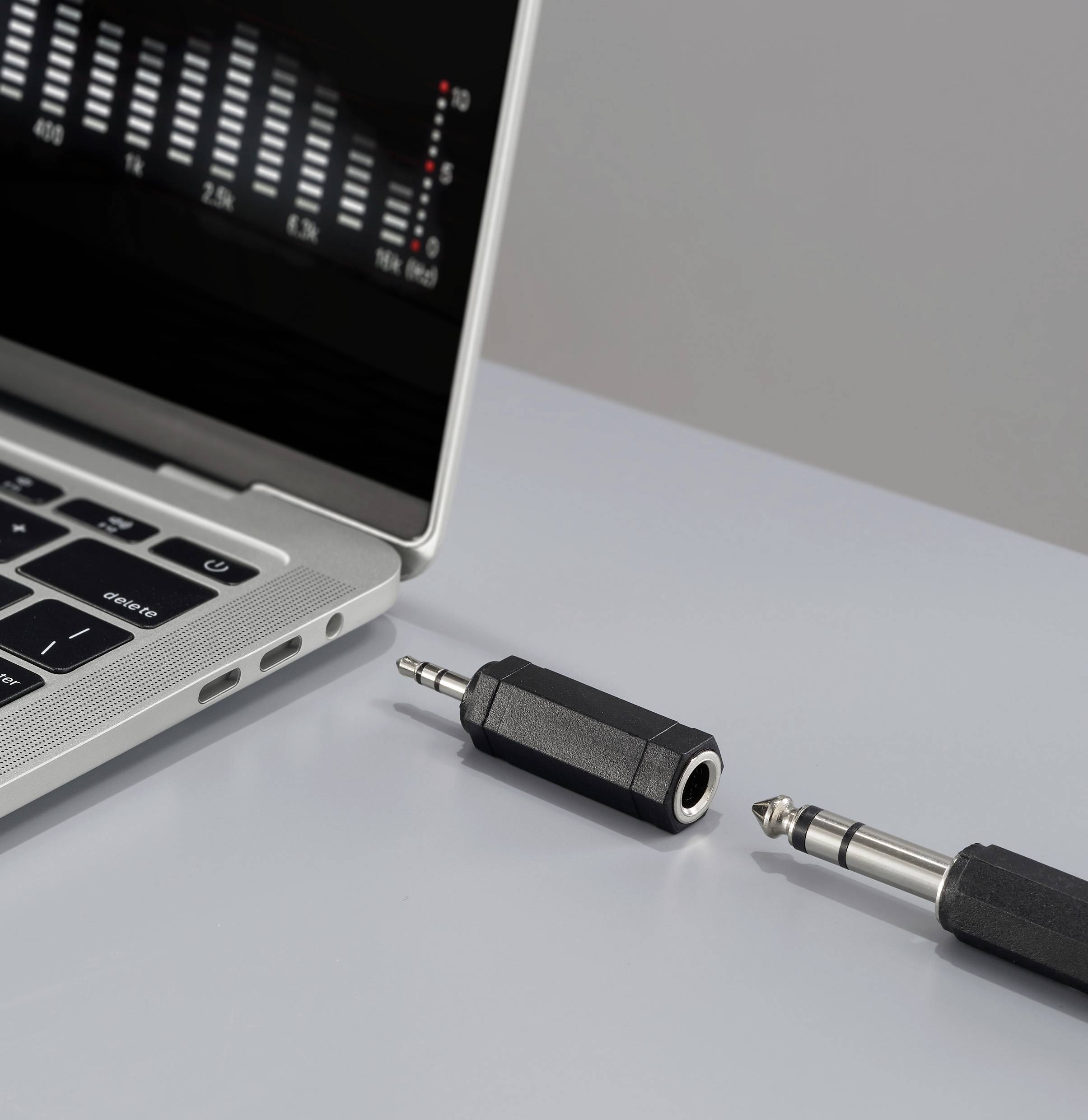 Ein Laptop mit einem geöffneten Audio-Mixer-Programm auf dem Bildschirm liegt neben einem 1/4-Zoll-Audioanschluss und einem Adapter auf einer grauen Oberfläche.
